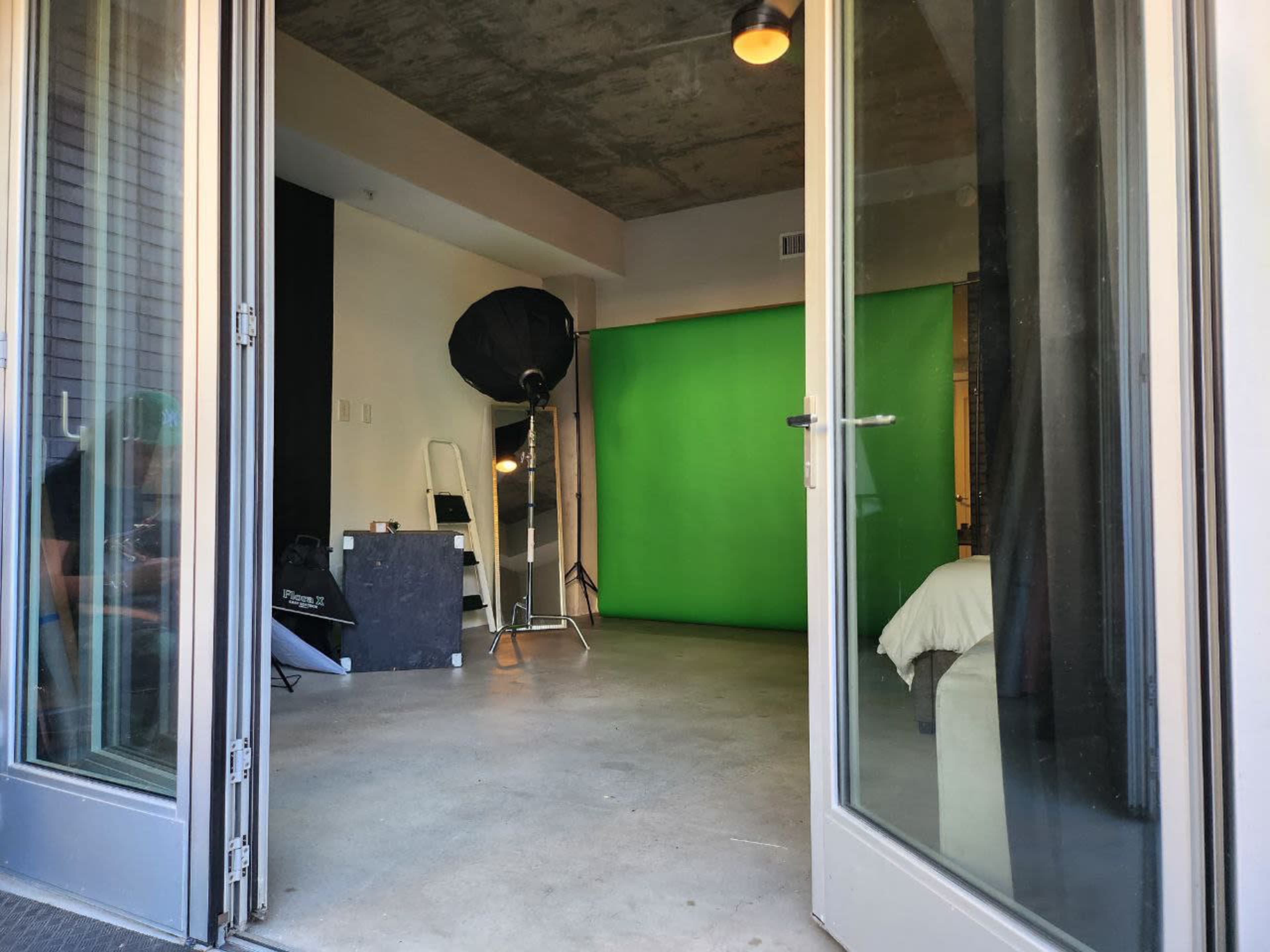 The image shows an empty studio space with a green backdrop, lighting equipment, and an open doorway that leads outside.
