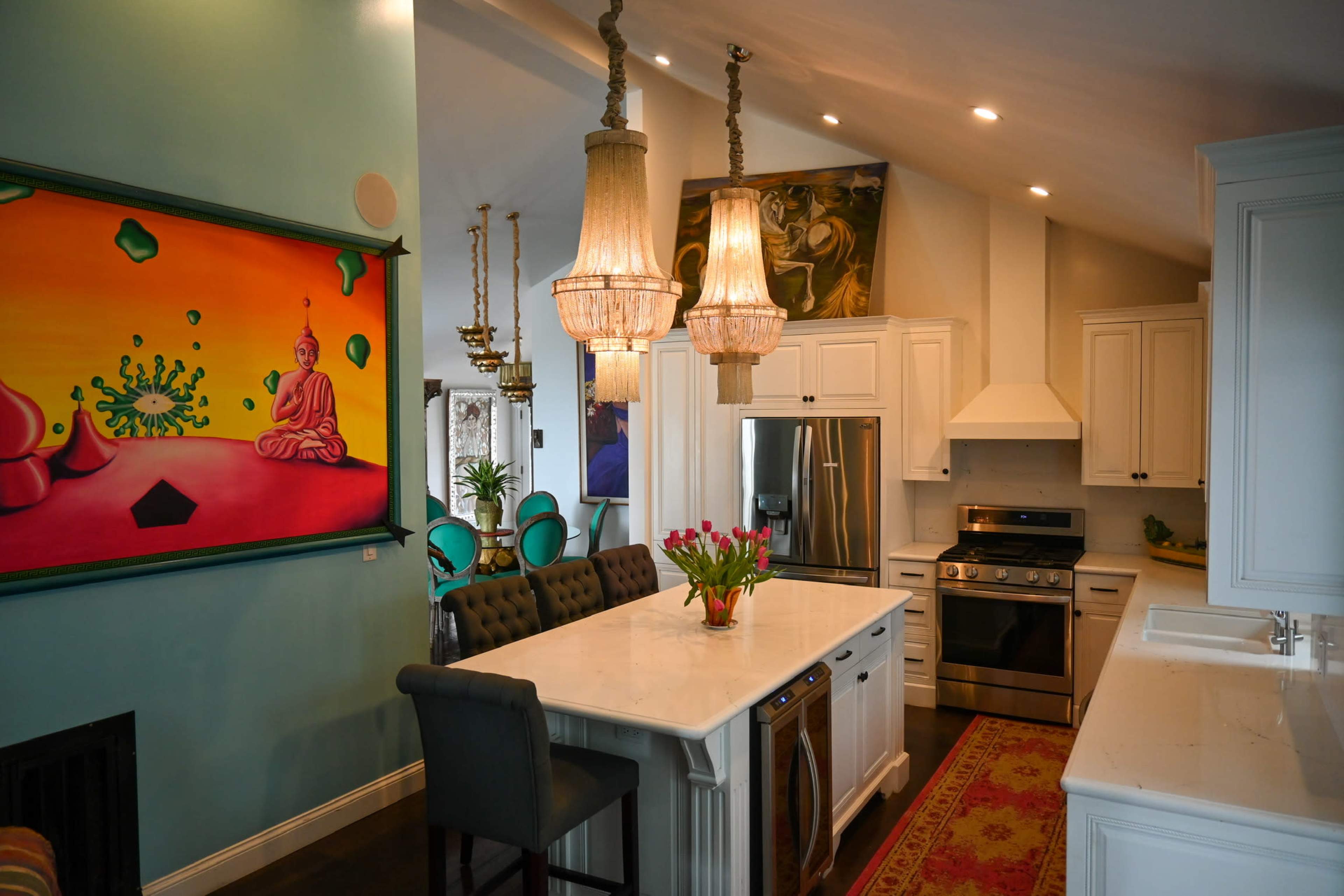 A modern kitchen features a central island with a marble countertop, stainless steel appliances, and vibrant artwork on the walls.