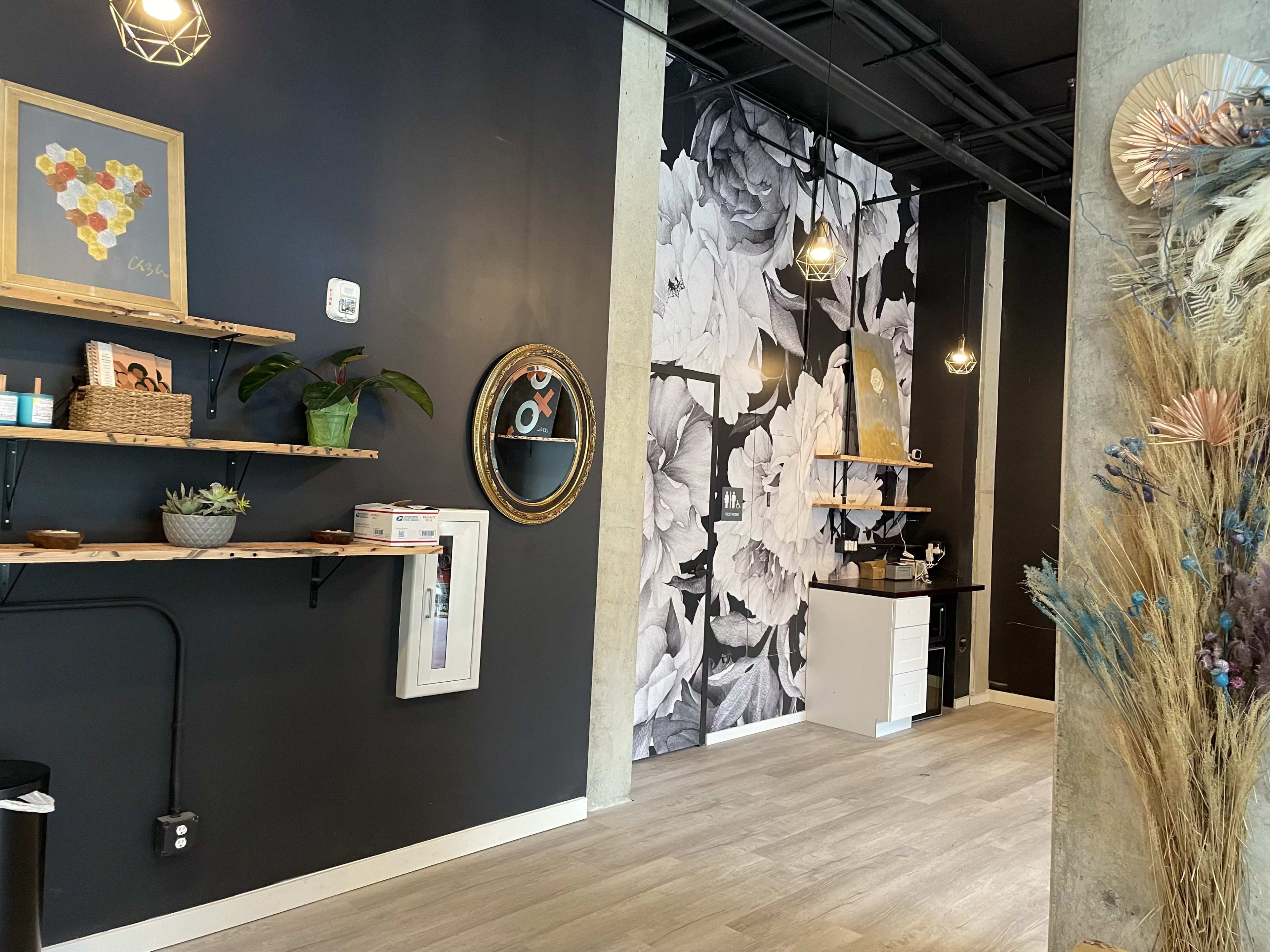 A modern interior space featuring black walls with floral wallpaper, wooden shelves displaying items, and a small white countertop.