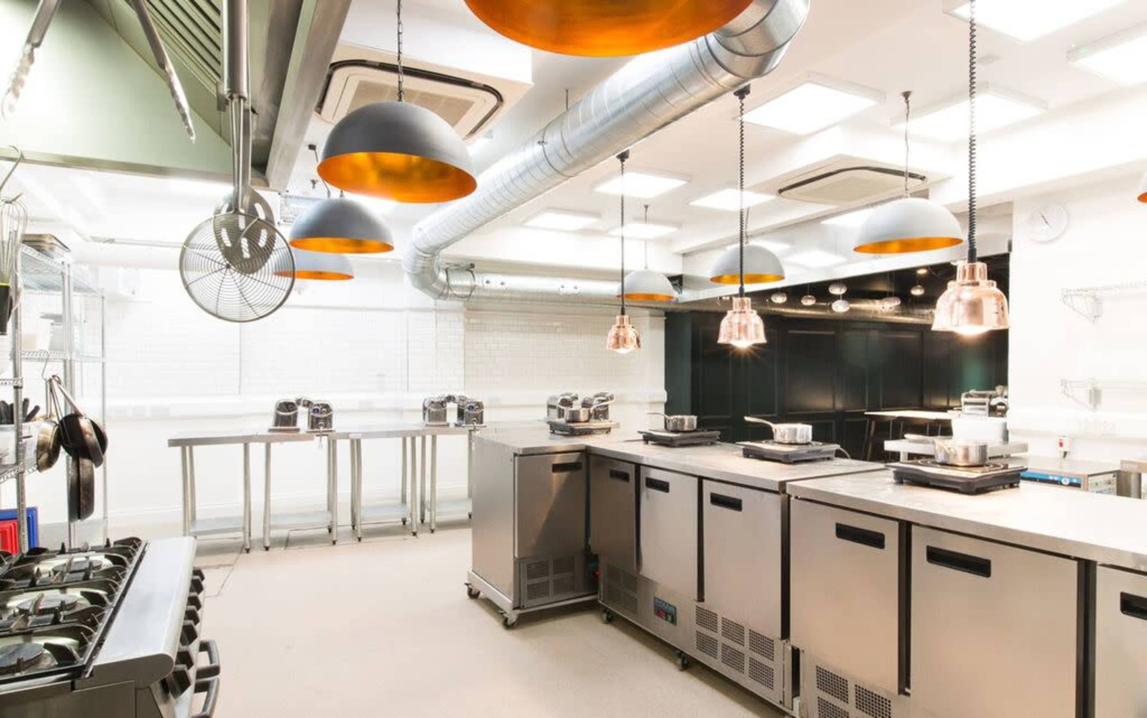 The image shows a modern kitchen equipped with stainless steel appliances, a central island, and hanging copper pendant lights.