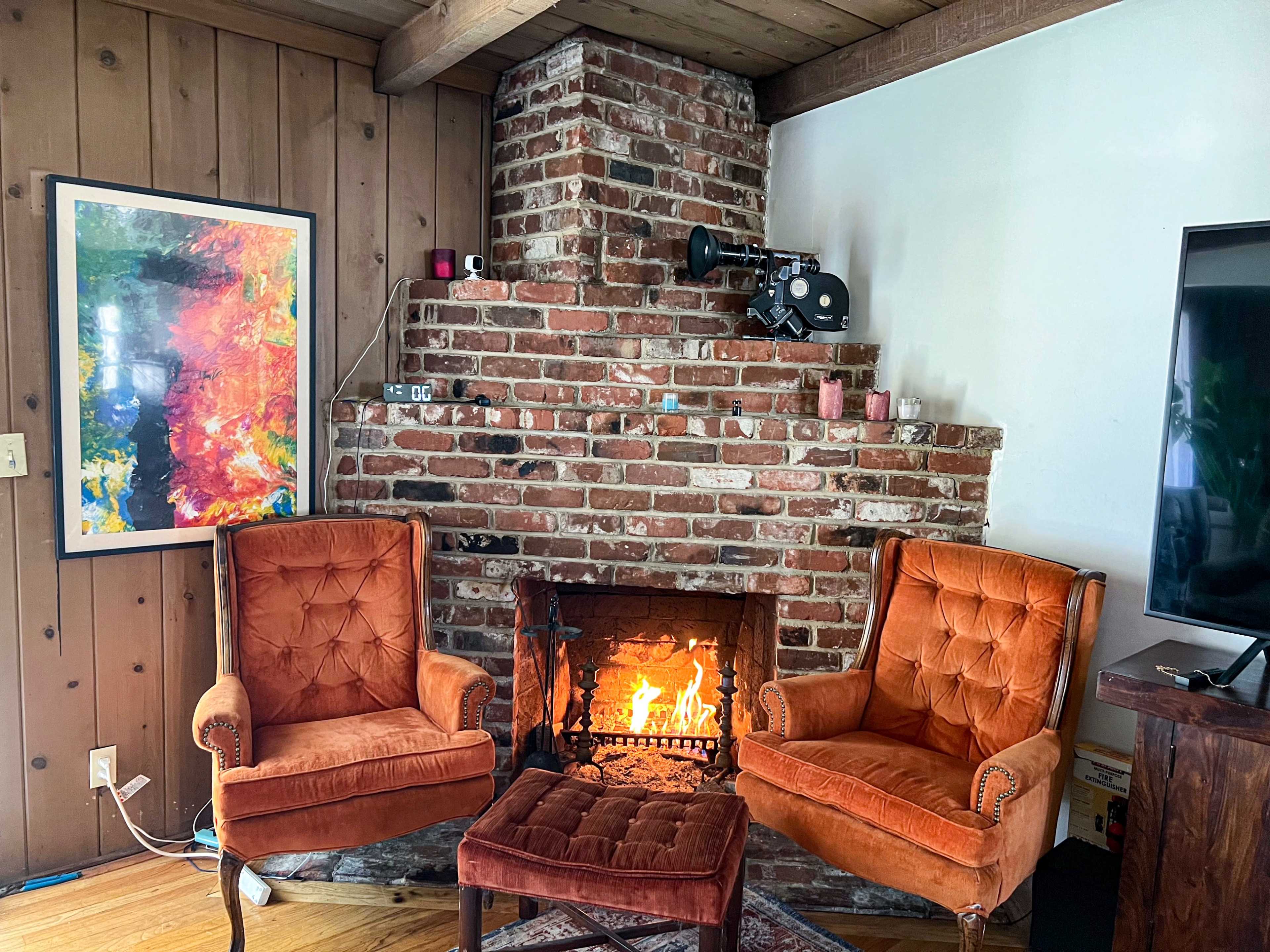 A cozy sitting area with two orange velvet chairs positioned near a brick fireplace, which has a small fire burning within it.
