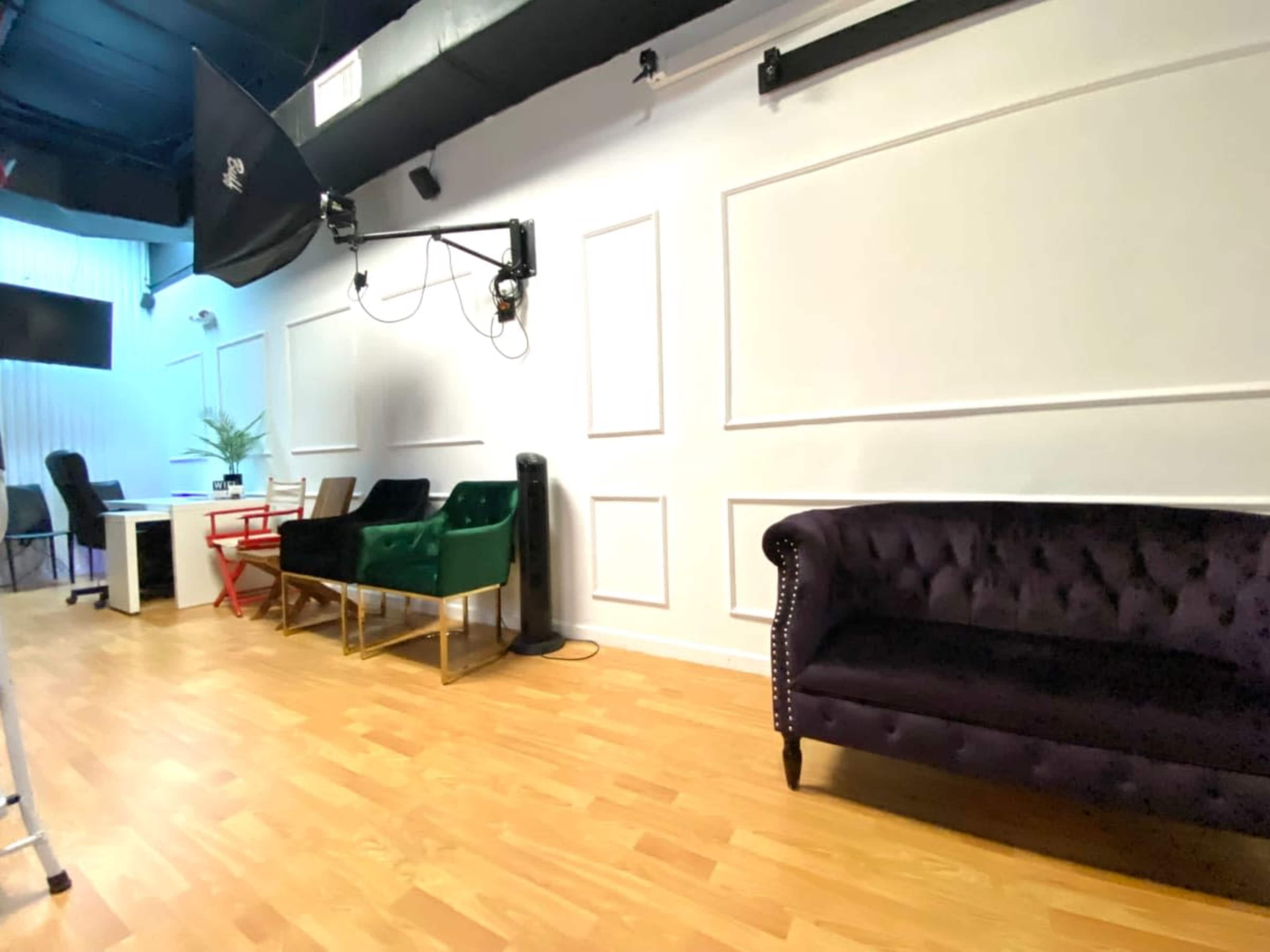 A modern studio space with a row of stylish couches against a white wall, wooden flooring, and studio lighting equipment above.