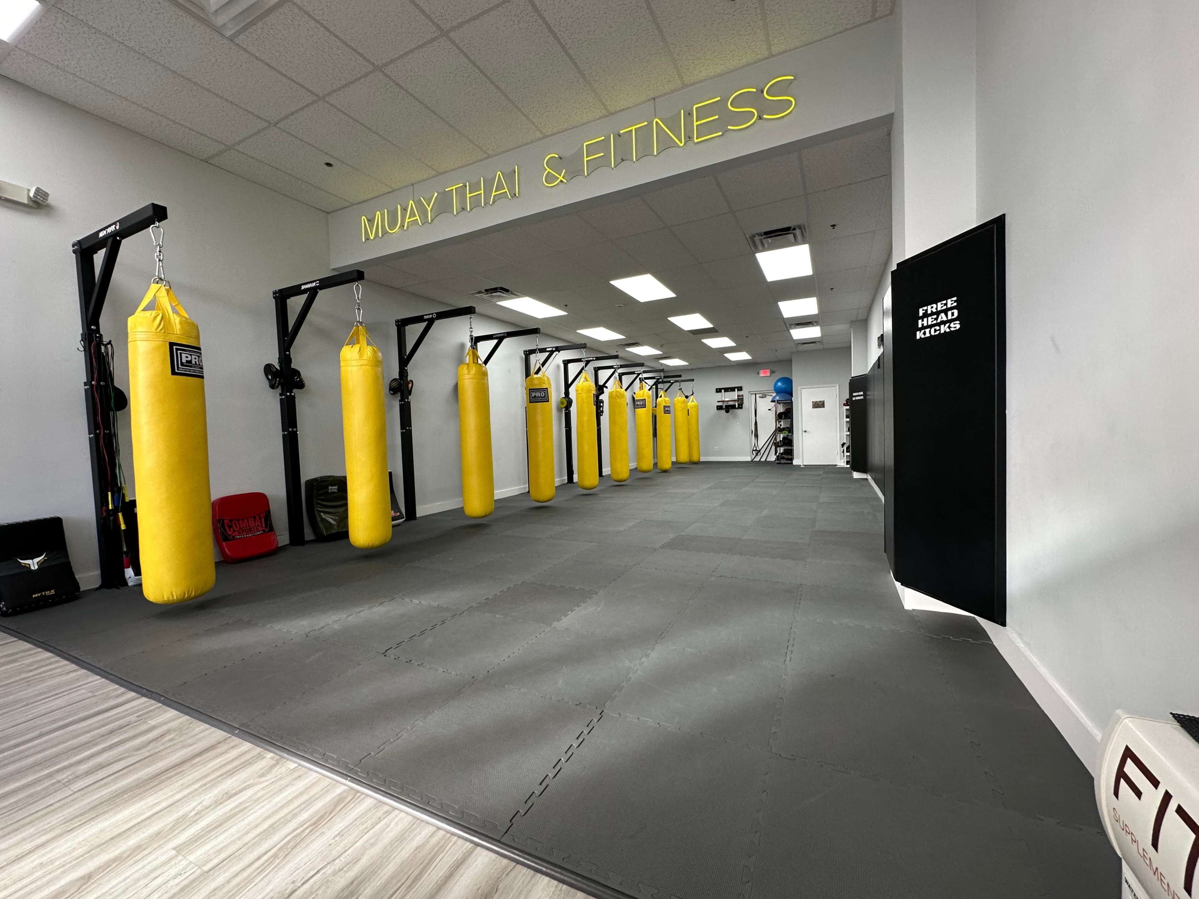 A spacious gym area for Muay Thai and fitness, featuring several yellow punching bags hanging from black frames along one side of the room.