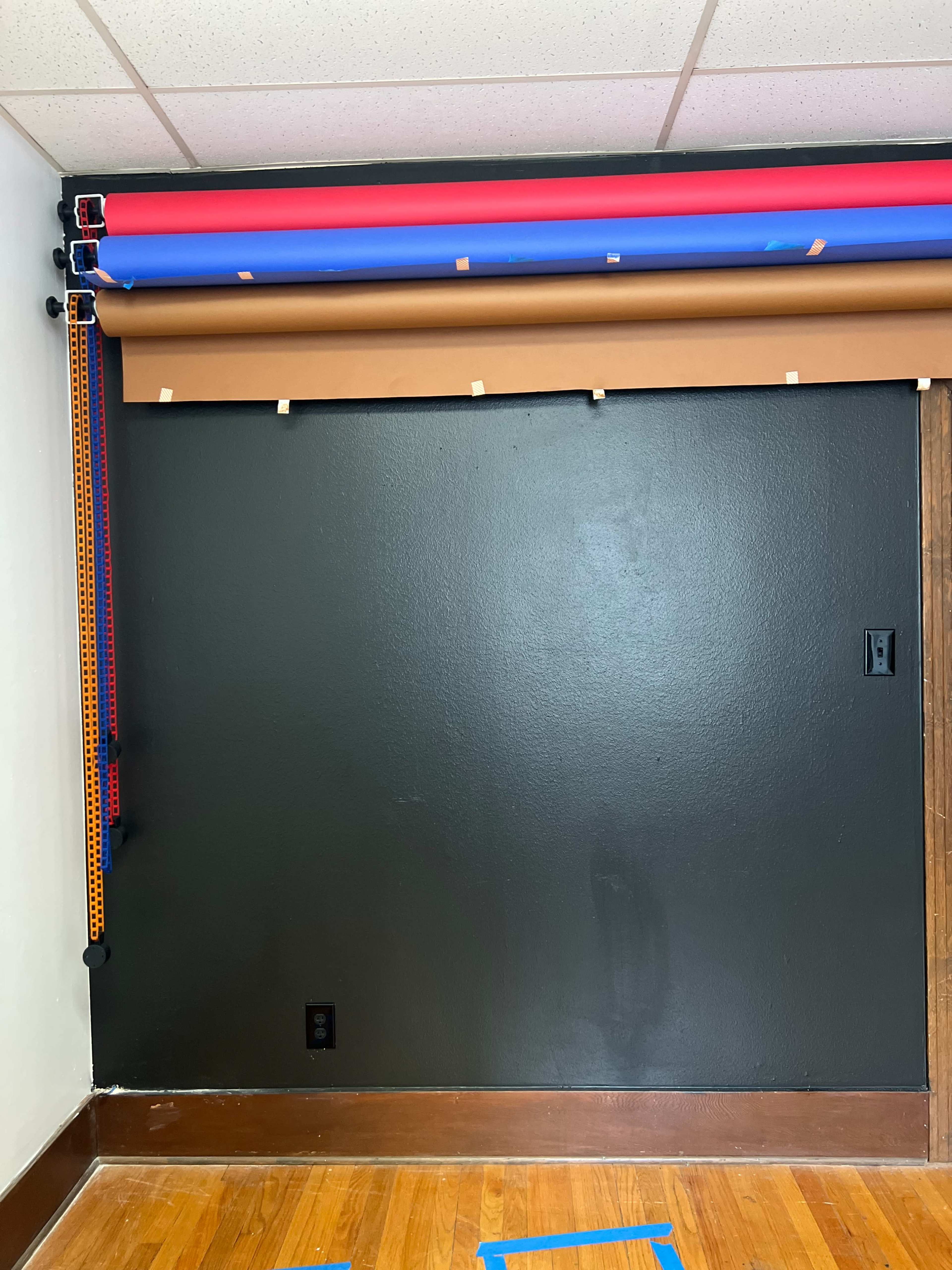 The image shows a wall painted dark green with rolls of colored backdrop paper stored above it.