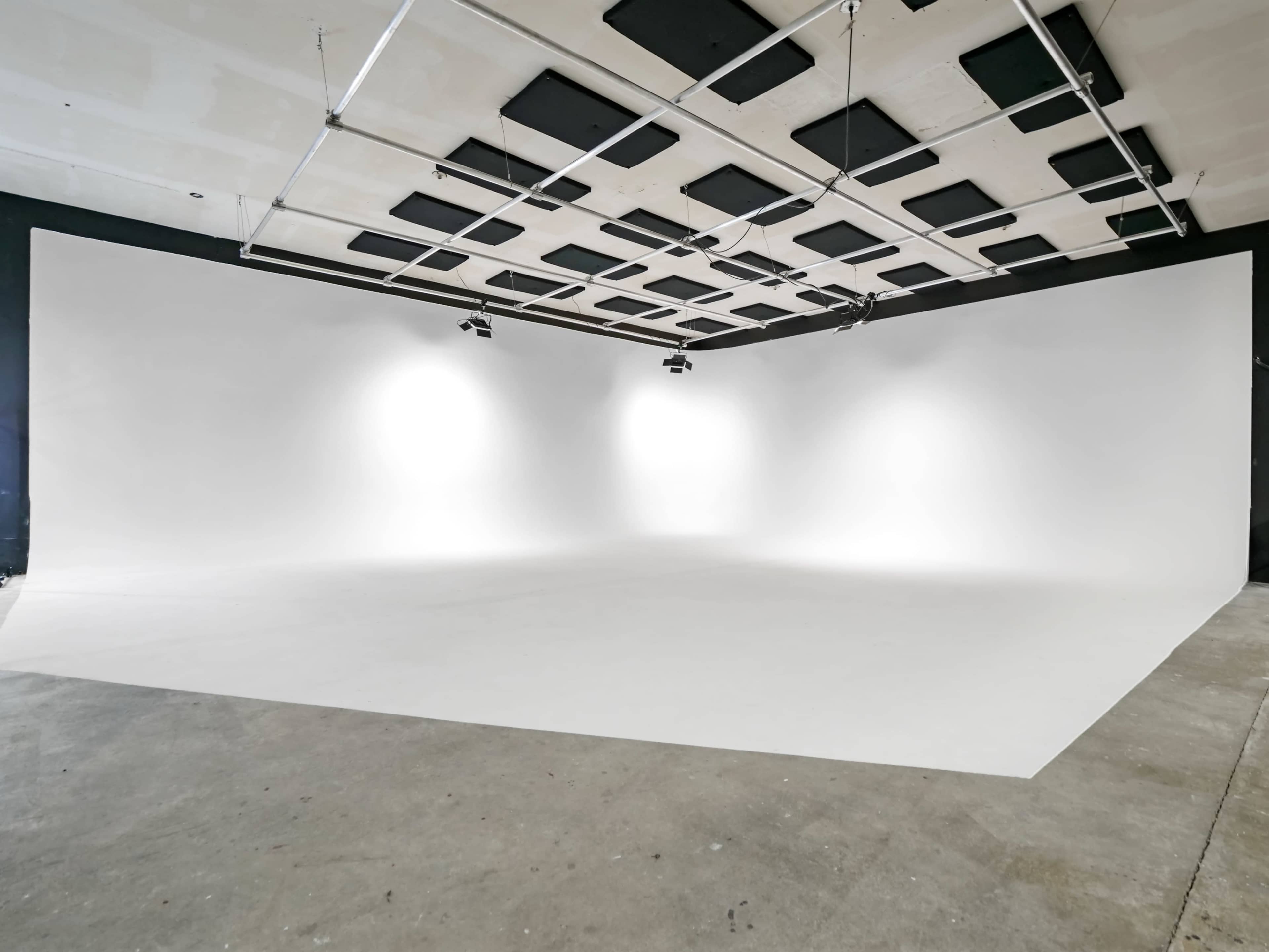 A spacious photo studio with white walls and a seamless backdrop, equipped with overhead lighting.