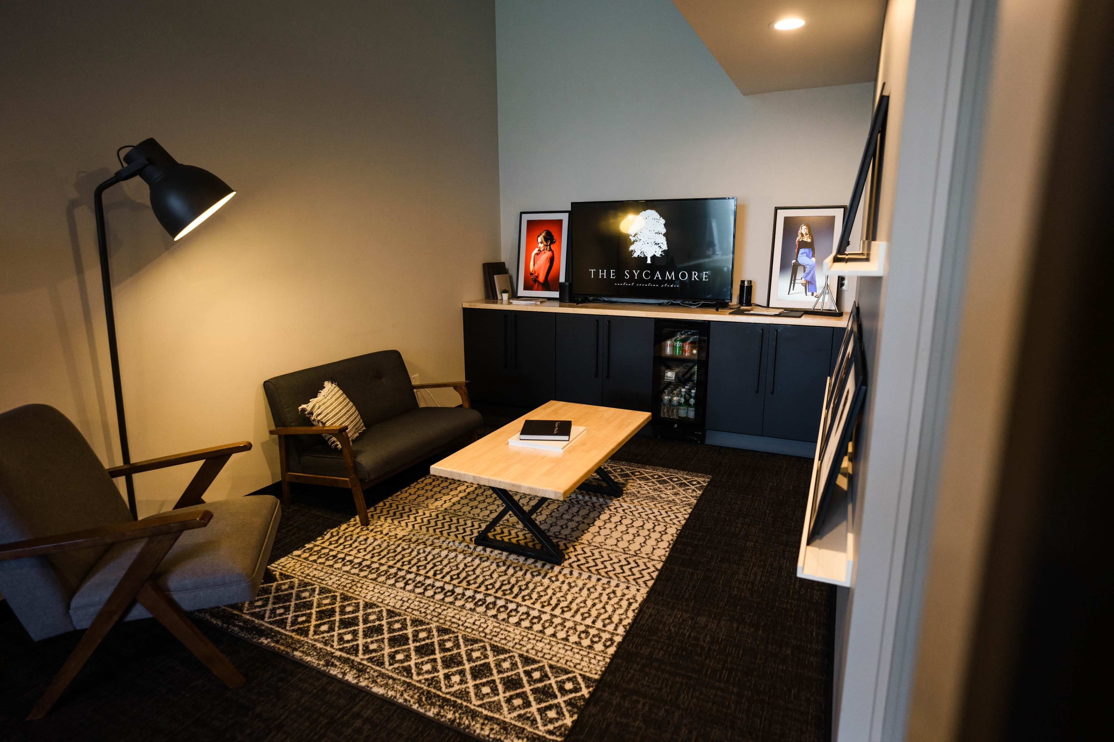 A small living area with a sofa, a chair, a coffee table, and a television mounted on a cabinet, all arranged on a patterned rug.