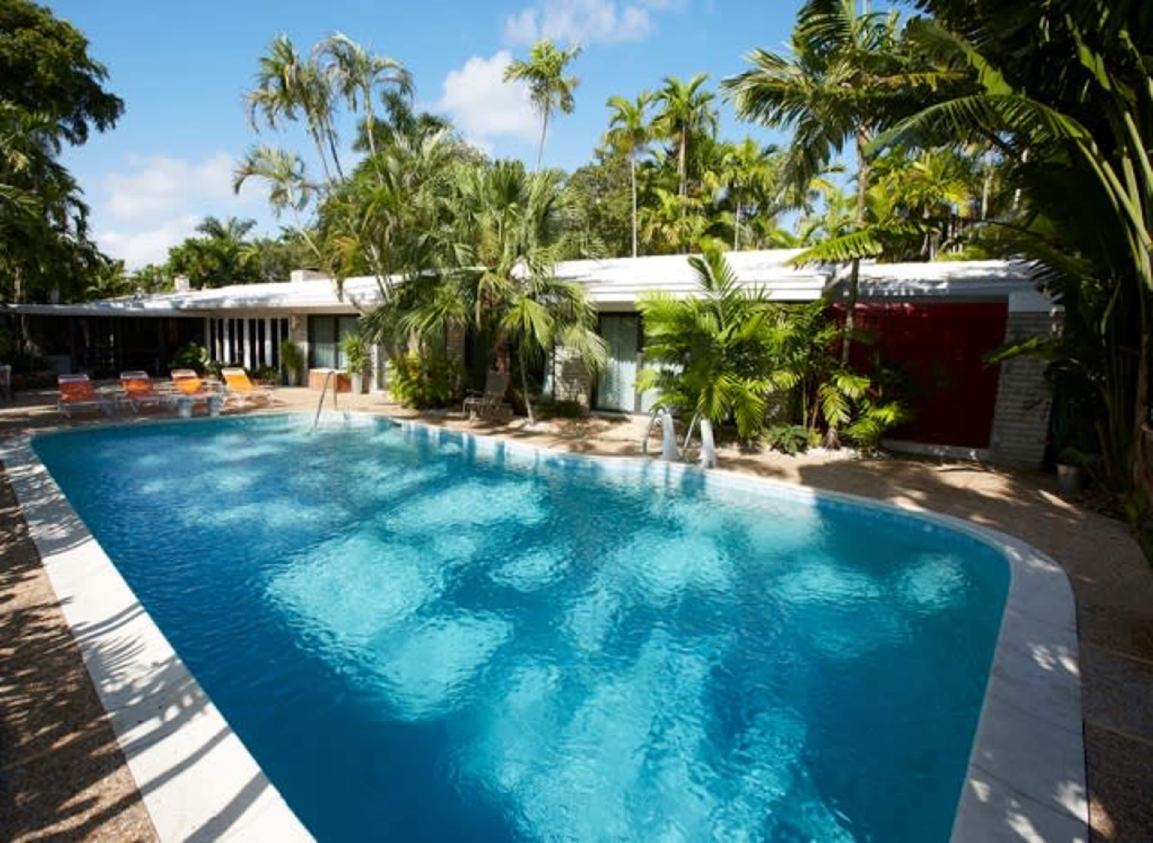A large swimming pool surrounded by tropical plants and a modern building in the background.