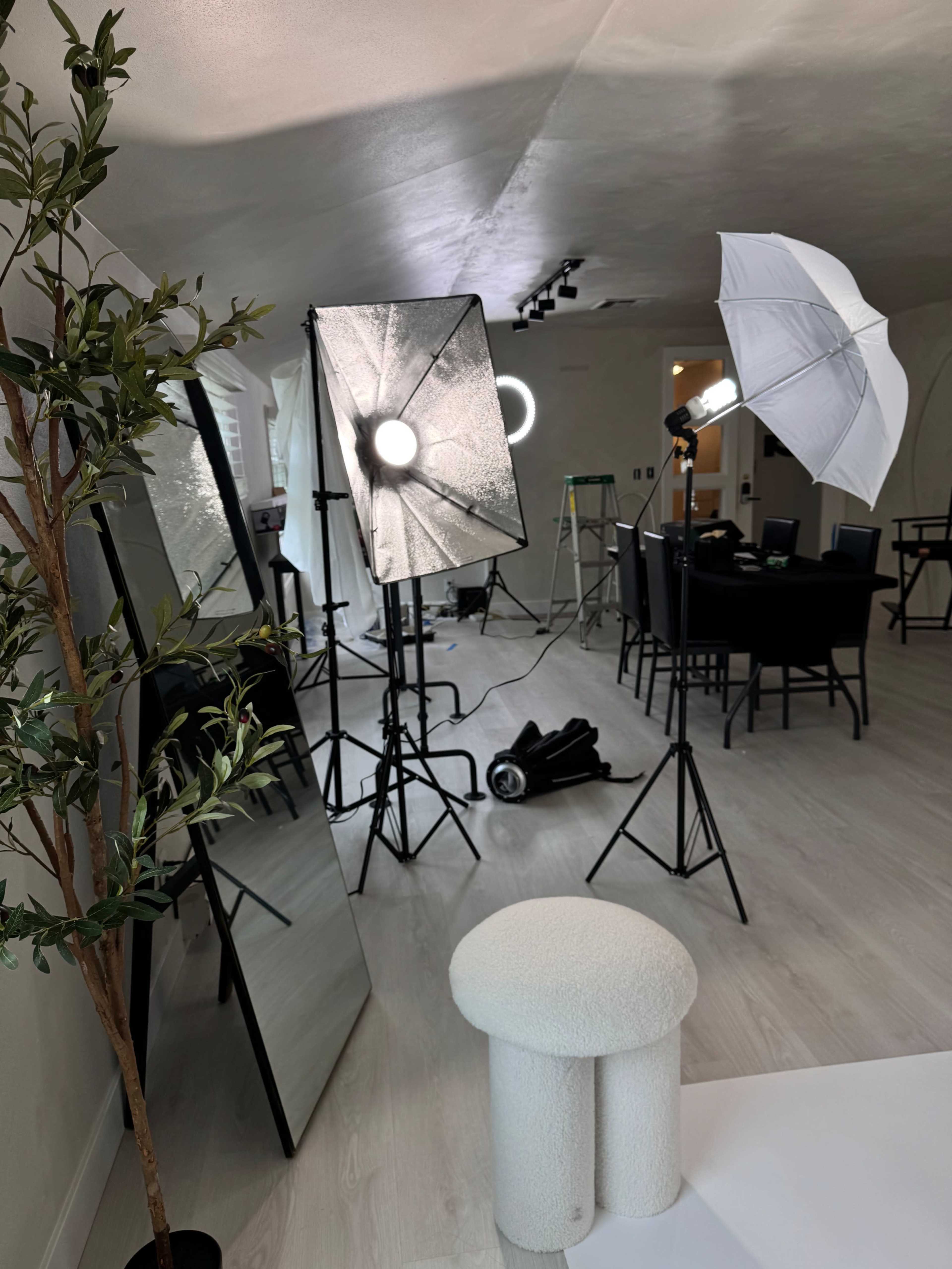 A photography setup with lighting equipment, a mirror, and a small stool in a spacious, bright room.