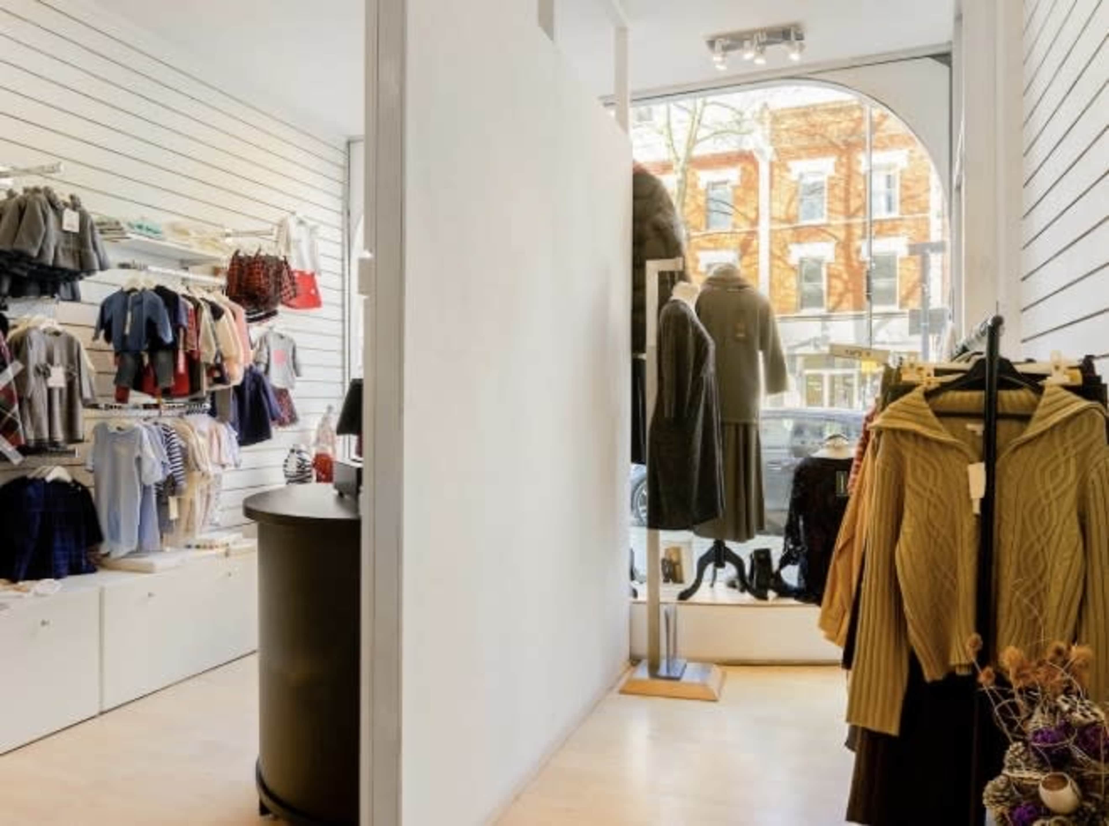 A retail store interior features clothing displays on the left and a large window that reveals a view of the street outside.