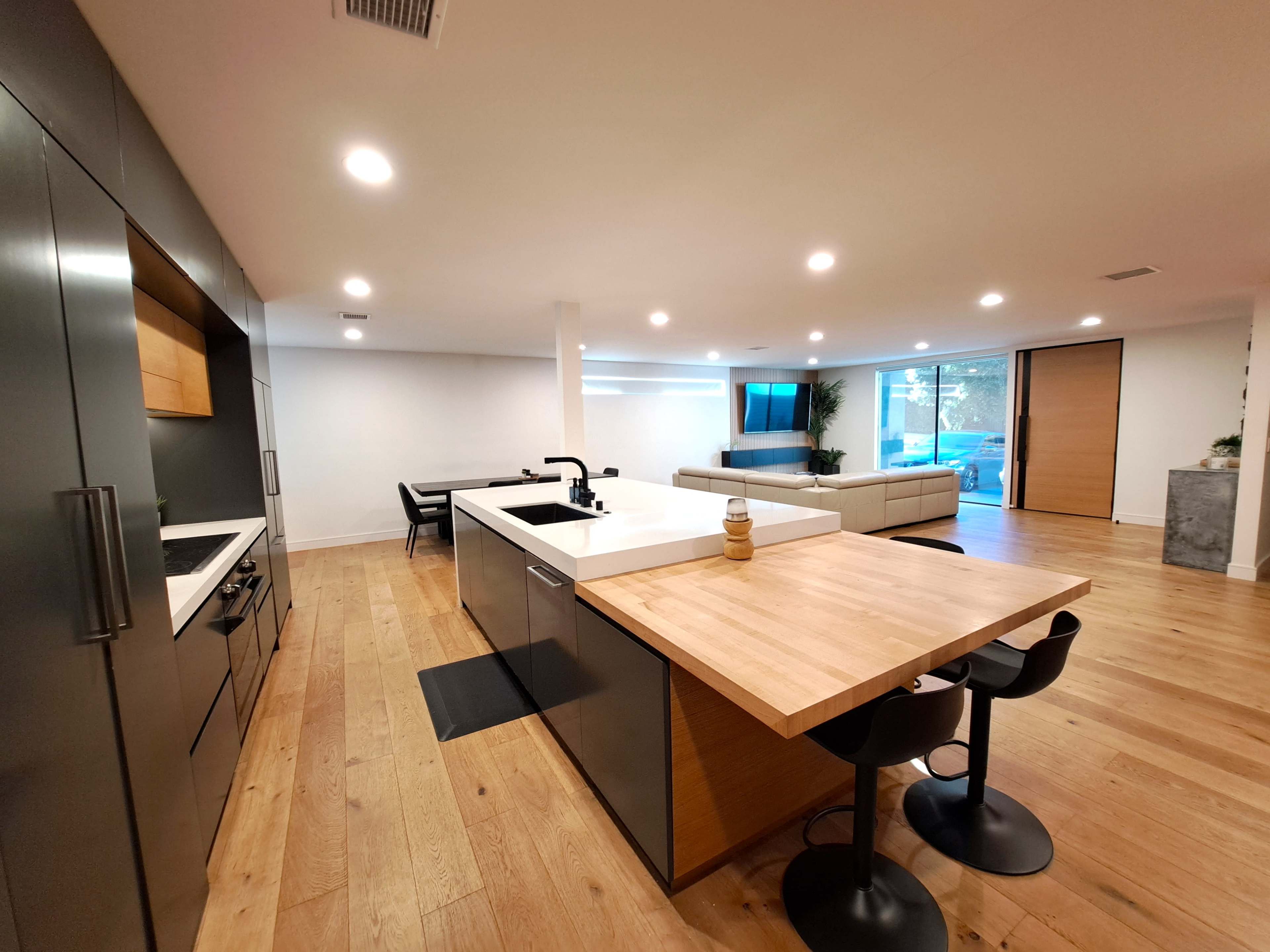 A modern kitchen connected to a spacious living area featuring an island with seating, sleek cabinets, and large windows.