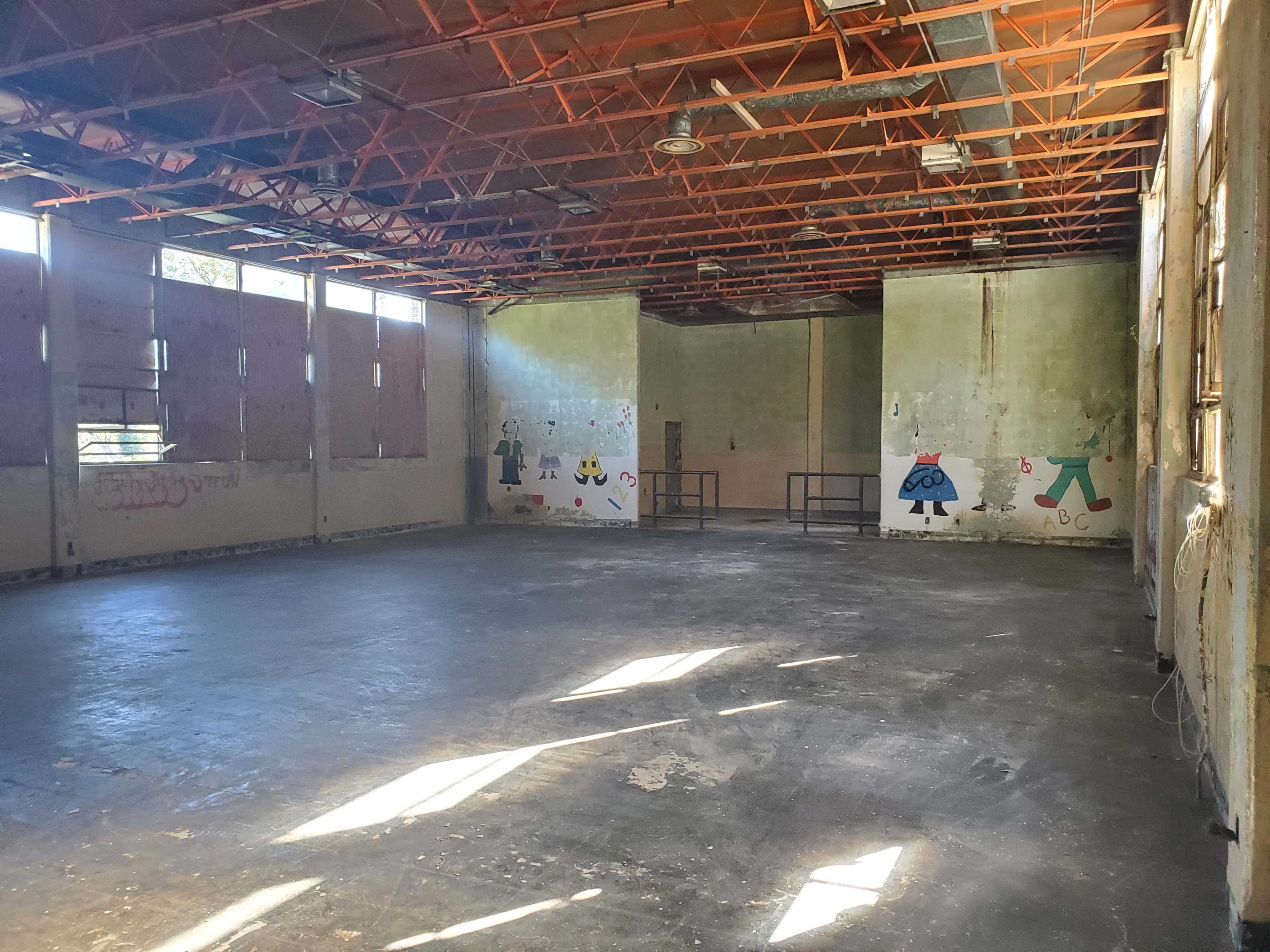 An empty, industrial-style room with a bare concrete floor and walls adorned with simple colorful murals.