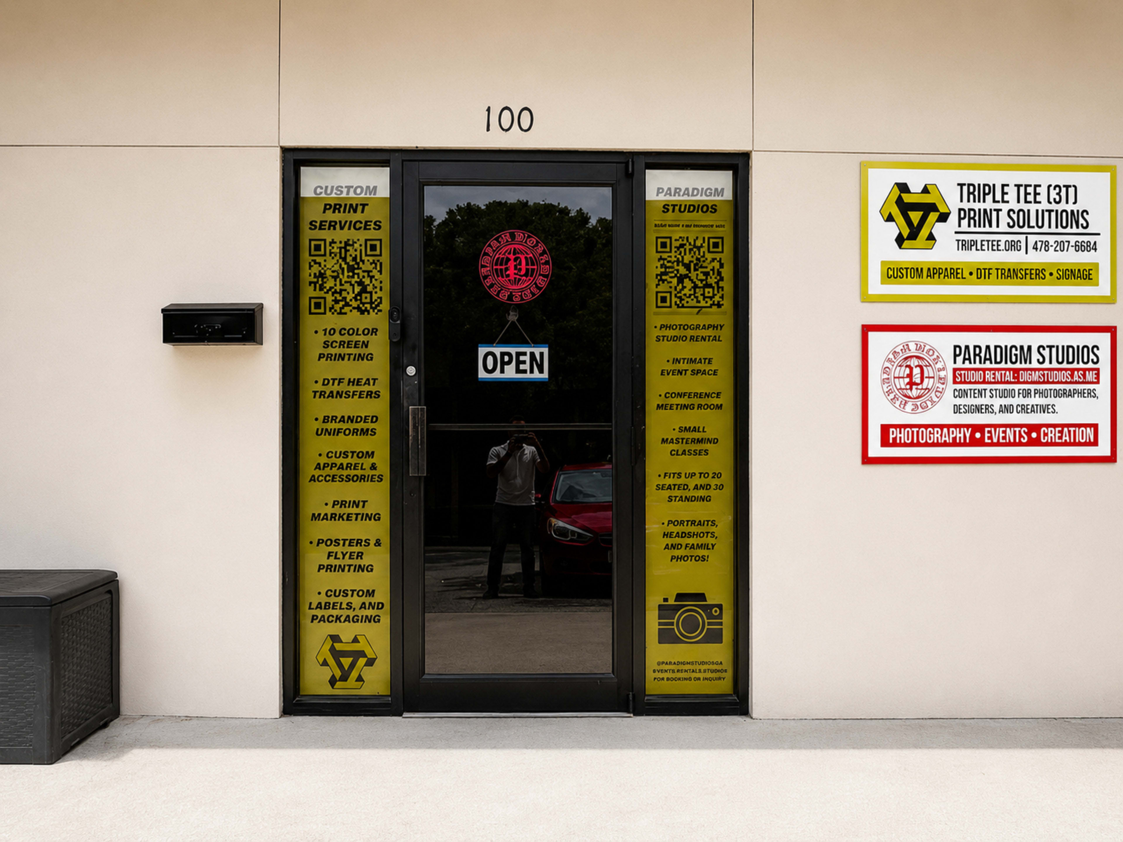 The image shows a storefront with a glass door labeled "Open," featuring multiple signs advertising custom print services, photography, and event creation.