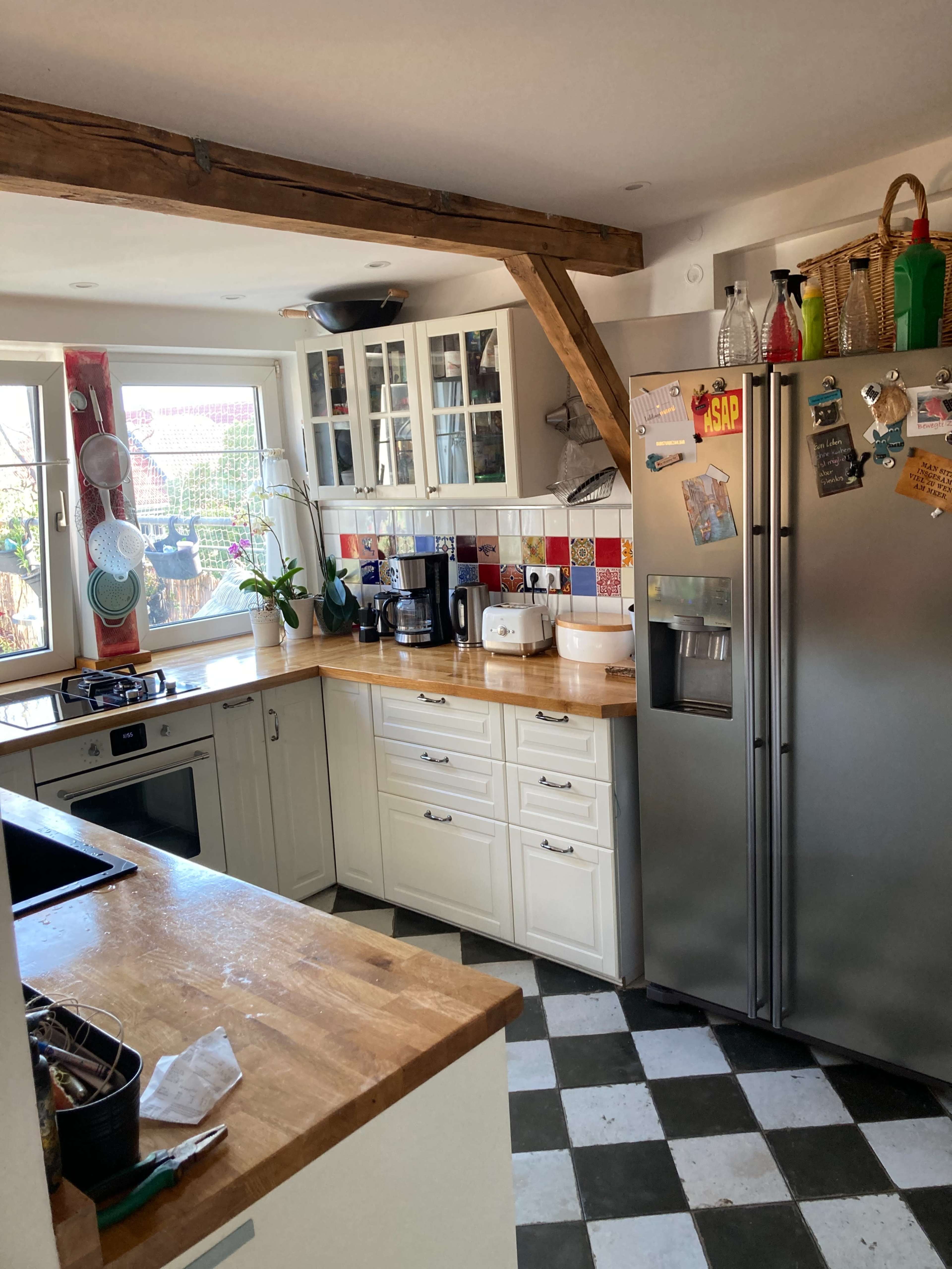 A bright kitchen features a wooden countertop, white cabinets, silver appliances, and a checkerboard floor.