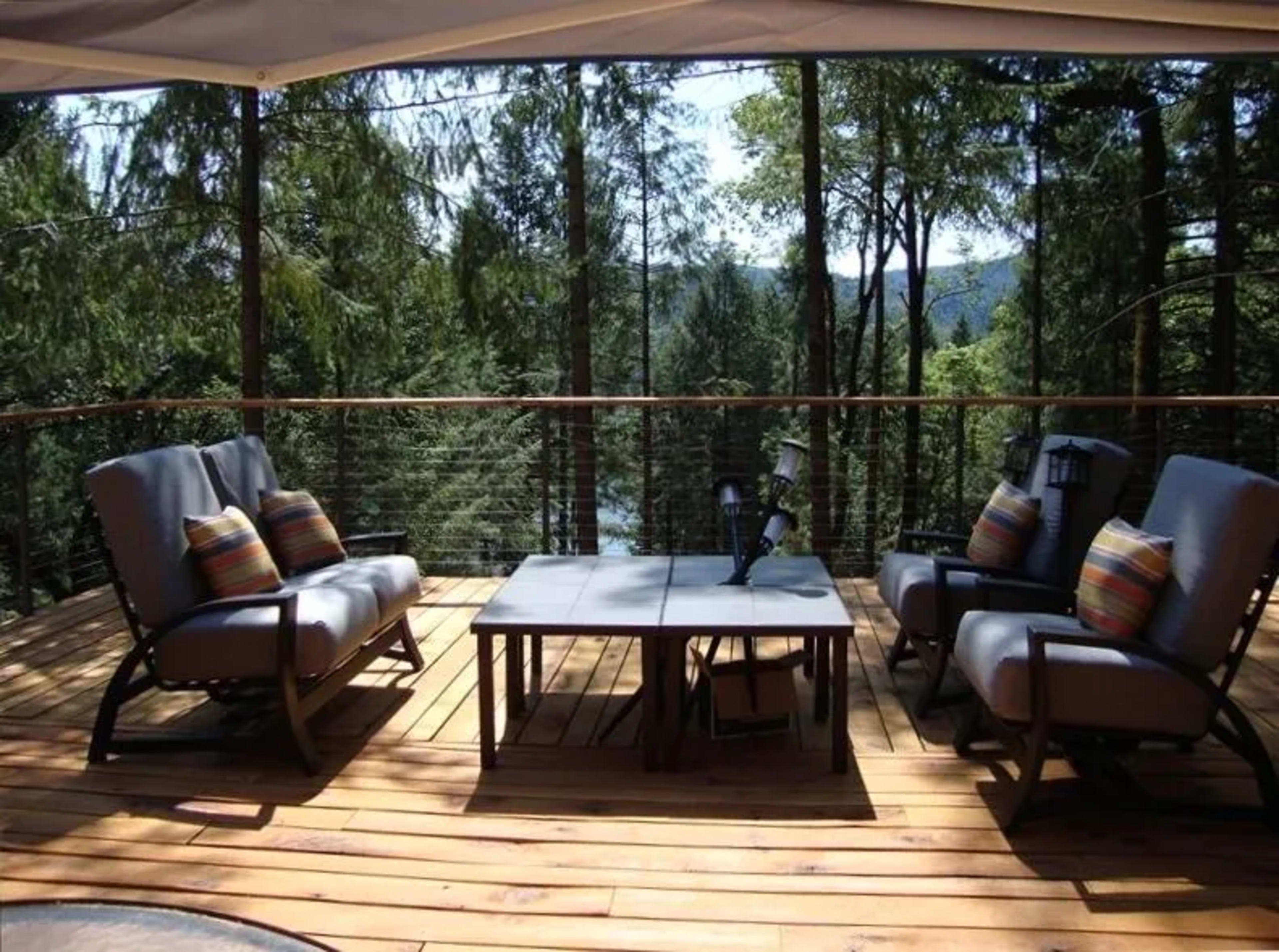 A wooden deck with two cushioned chairs and a table overlooks a forested area.