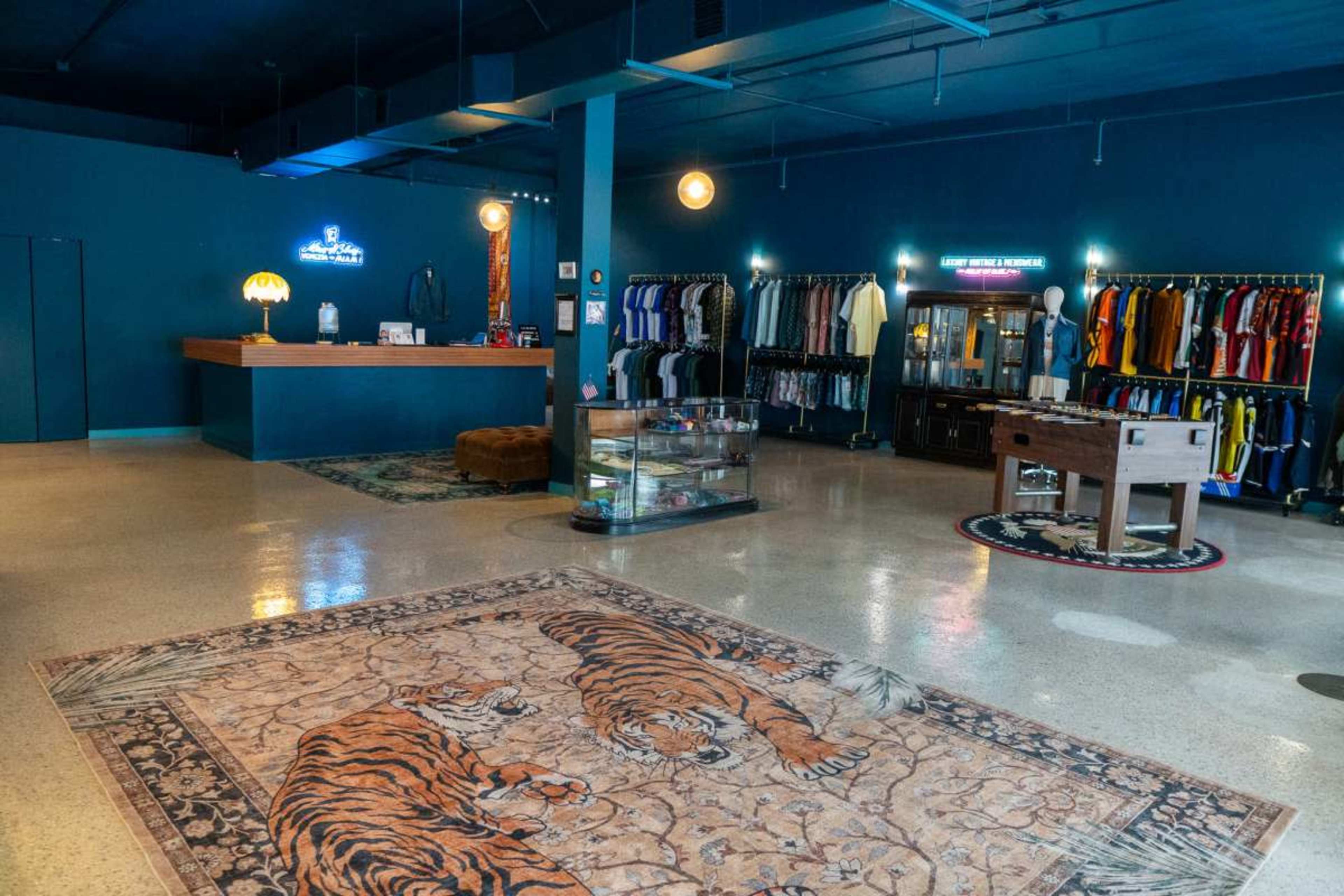 The image shows an interior retail space featuring a prominent area rug with tiger motifs, clothing displayed on racks against a blue wall, a reception counter, and display cases.
