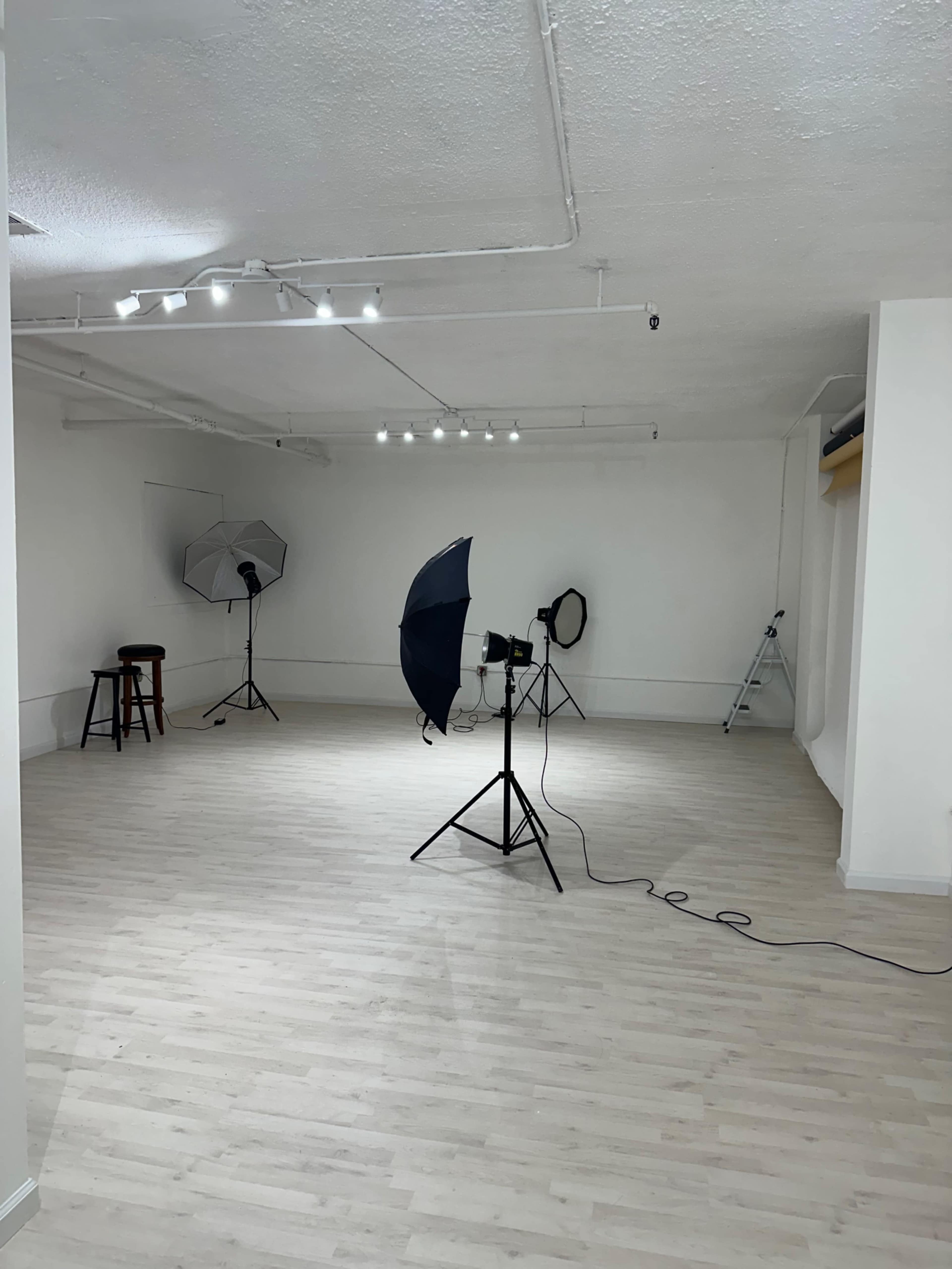 The image shows a spacious, empty photography studio equipped with various lighting setups and a ladder in the background.