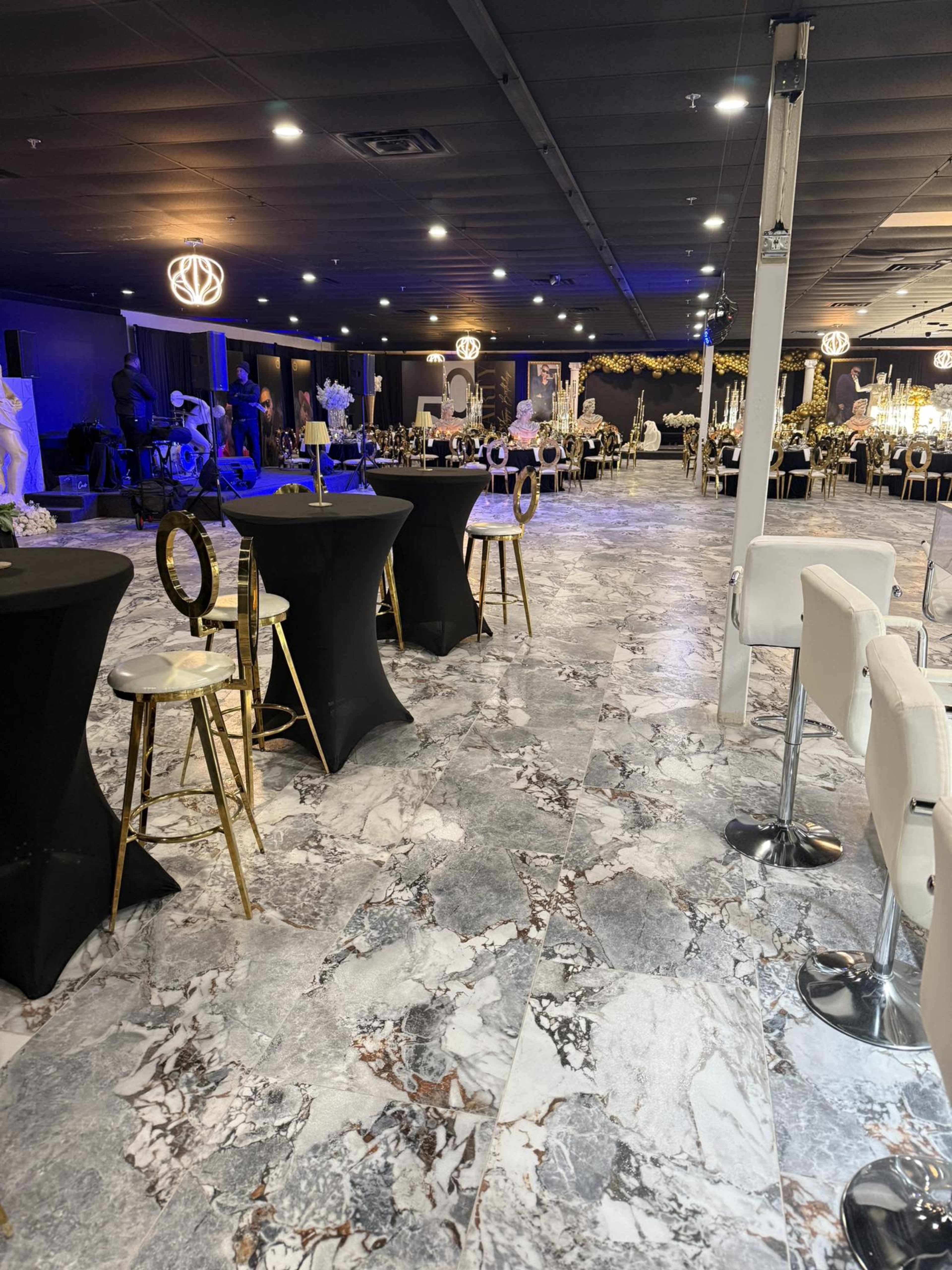 The image shows an upscale event space with marble flooring, black cocktail tables, and elegant seating arrangements, decorated for a gathering.