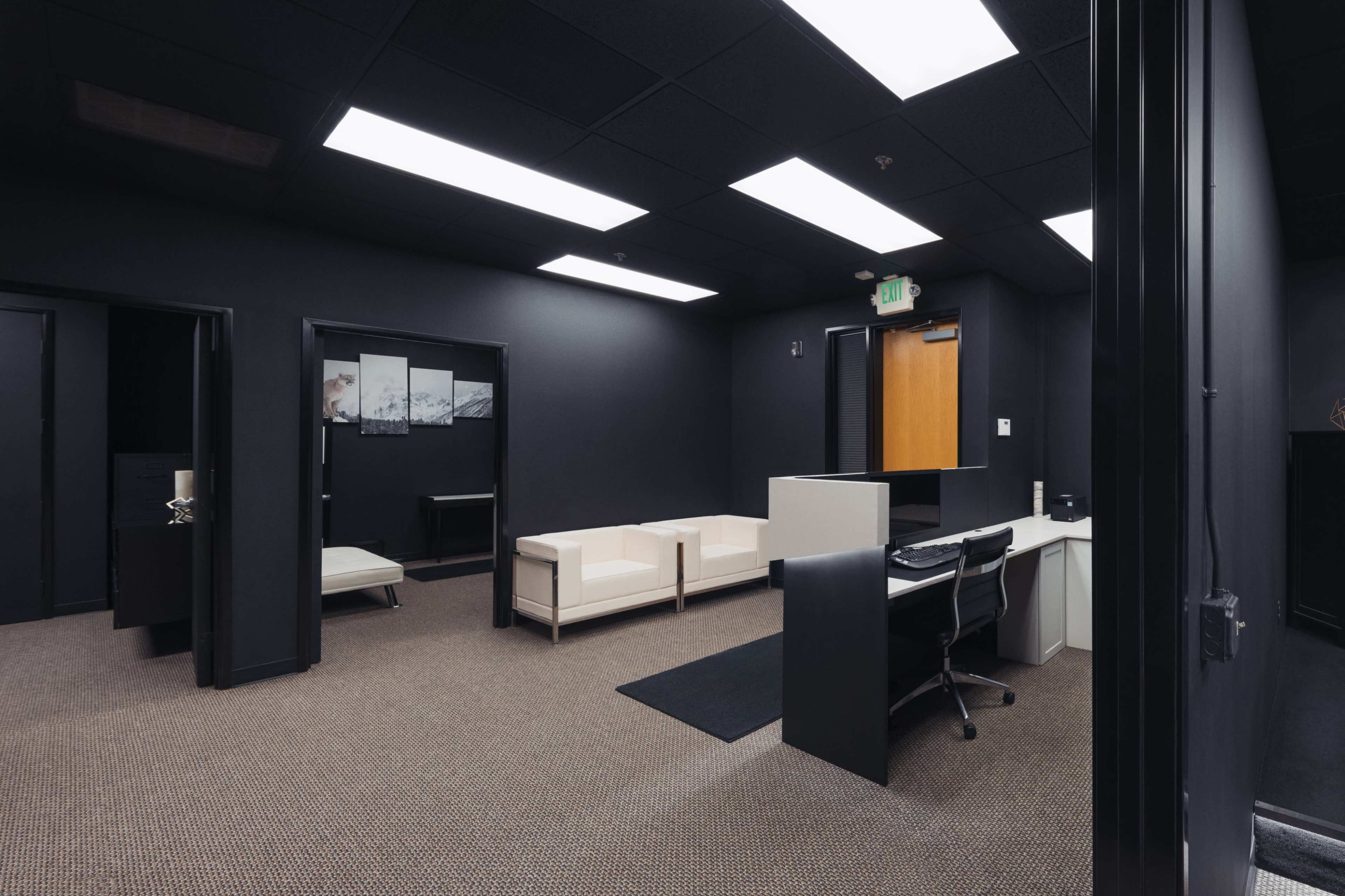 A modern office space featuring a reception area with a white desk, seating area with a white couch, and dark walls.