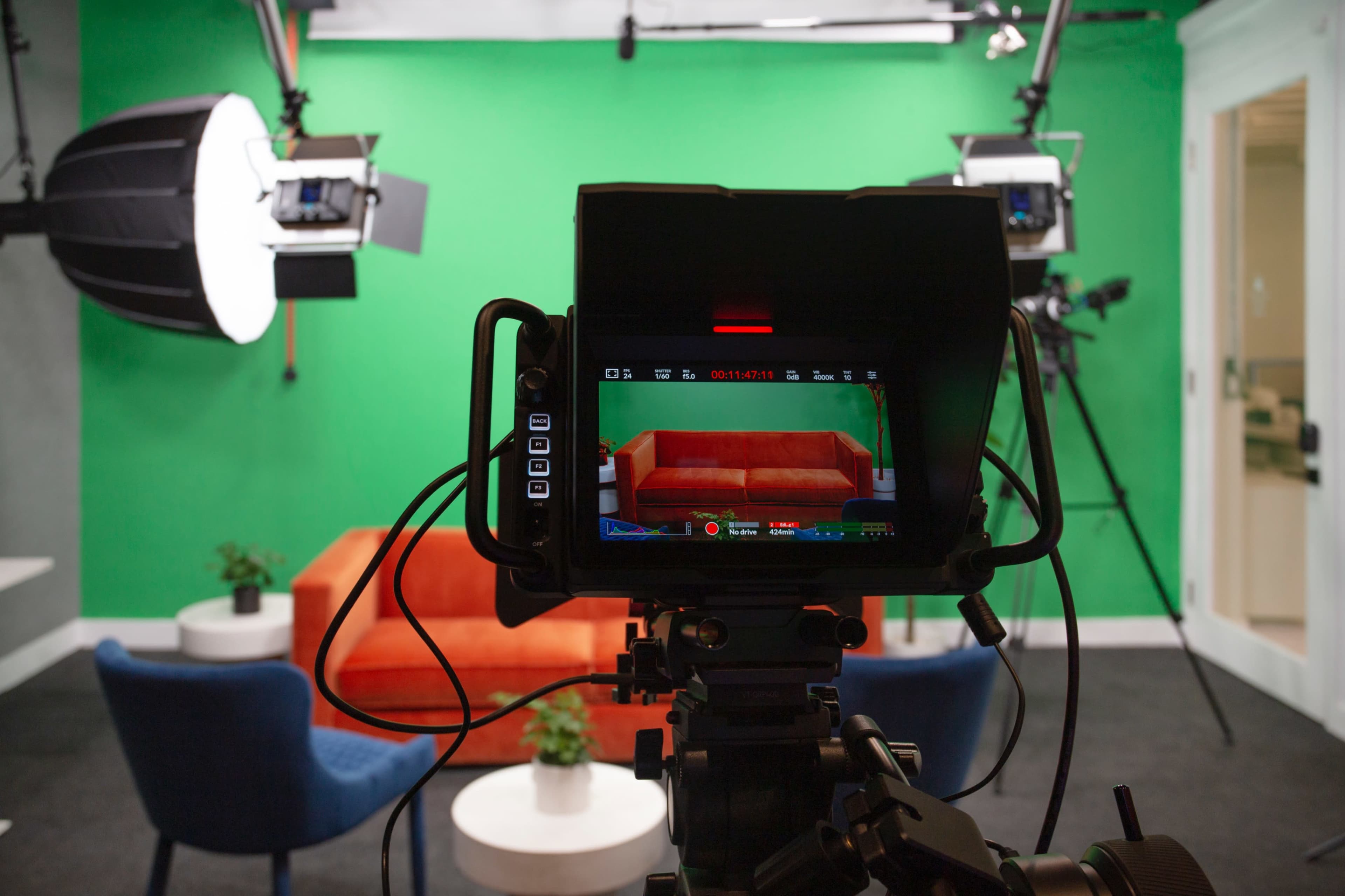 A camera is aimed at a brightly colored couch in a studio setup with green walls and professional lighting.