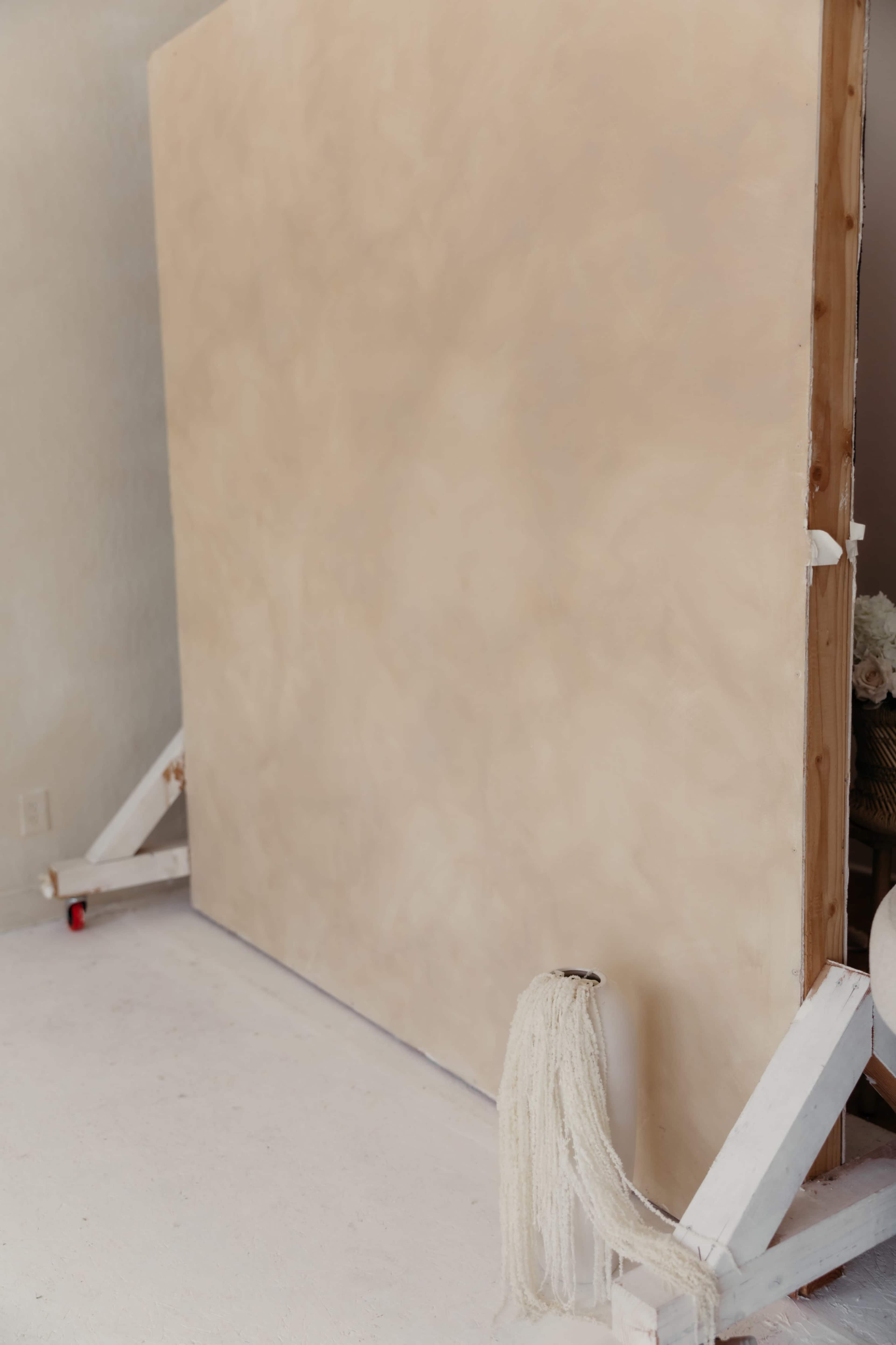 A large, blank, textured beige backdrop stands on a wooden frame in a light-colored studio space.