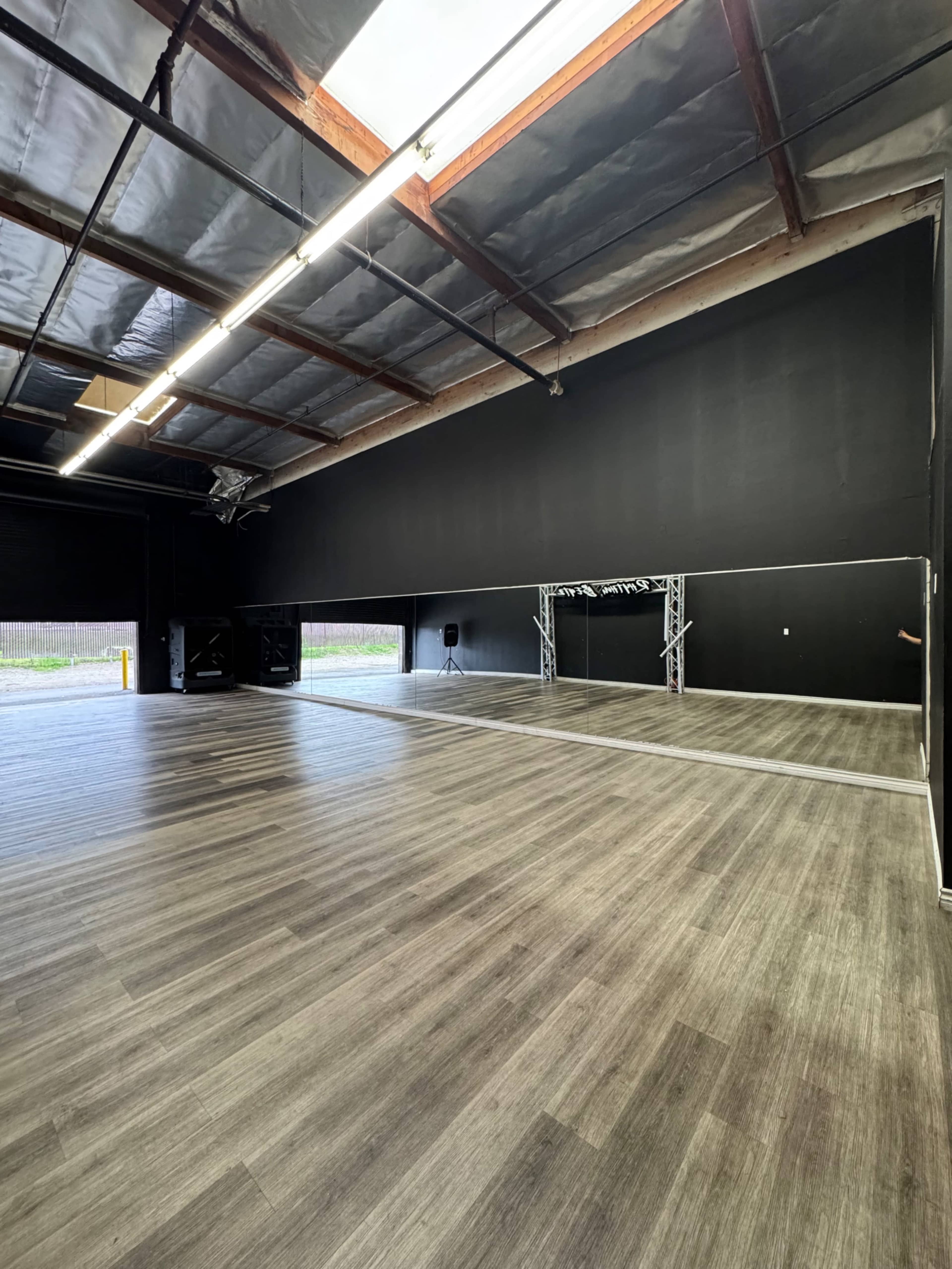 The image shows an empty dance studio with dark walls, wooden flooring, and a large mirror along one side.