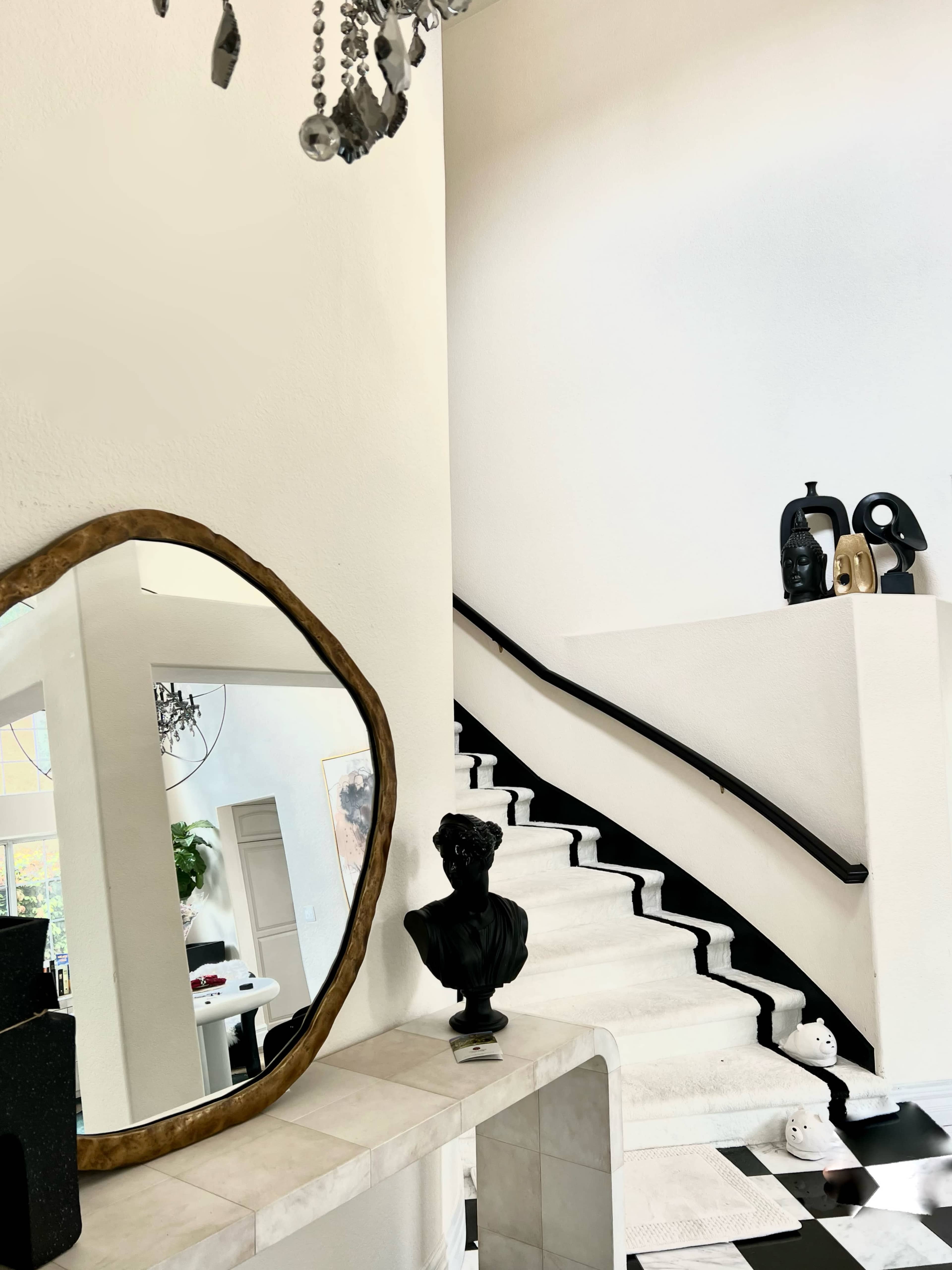 A modern entryway featuring a staircase, a large mirror, and a decorative bust on a console table.