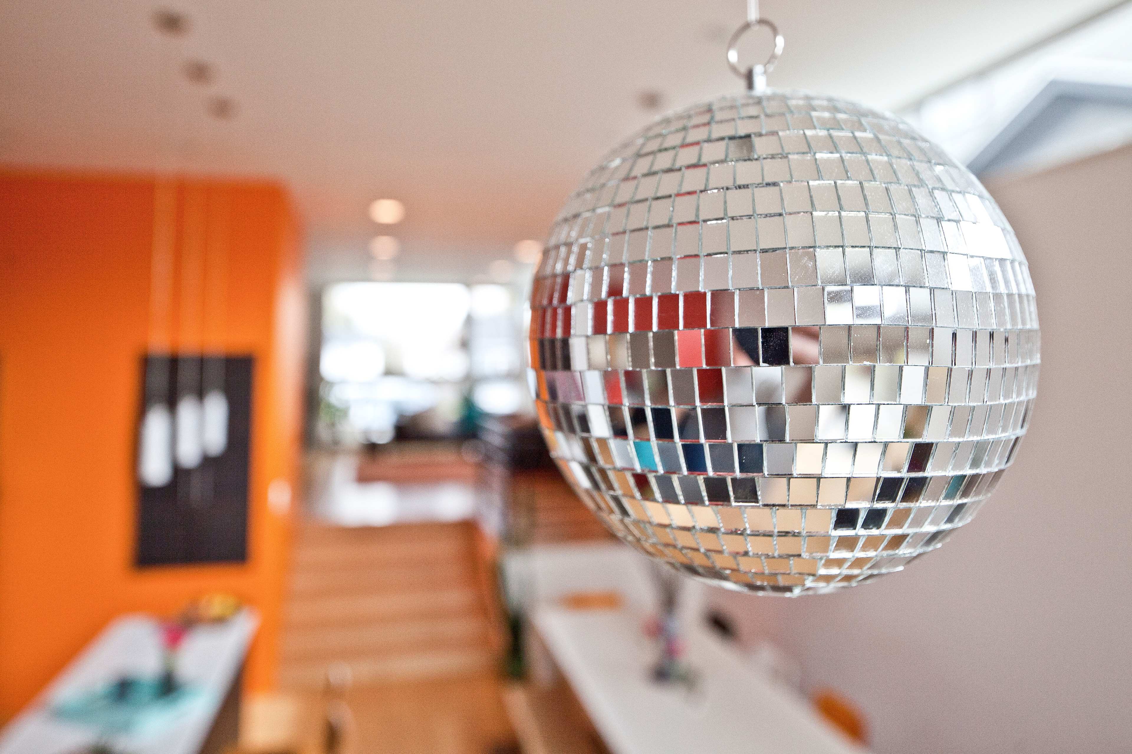 A reflective disco ball hangs from the ceiling in a brightly colored room with a wooden staircase in the background.