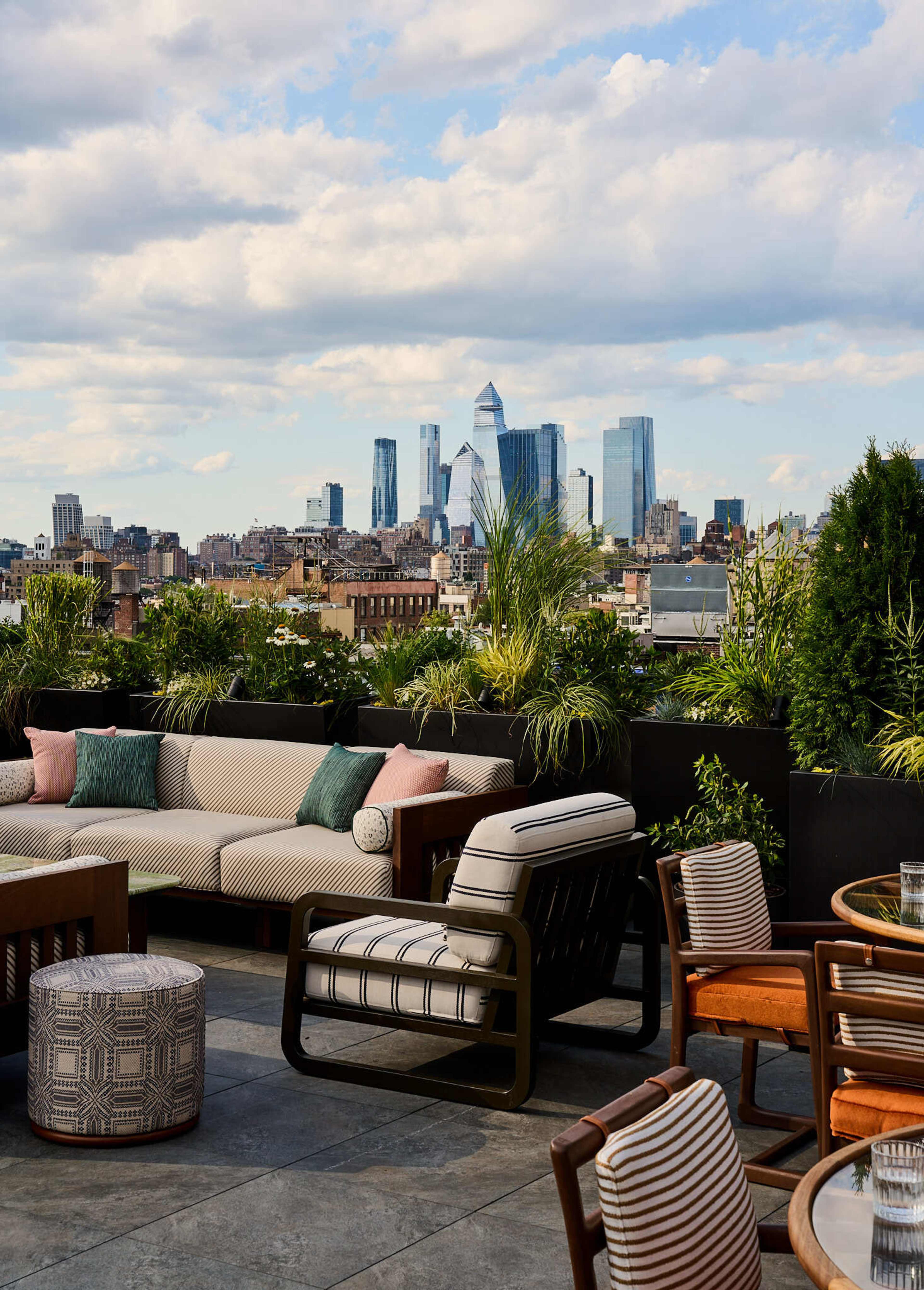 A rooftop terrace features modern seating and lush greenery with a city skyline in the background.