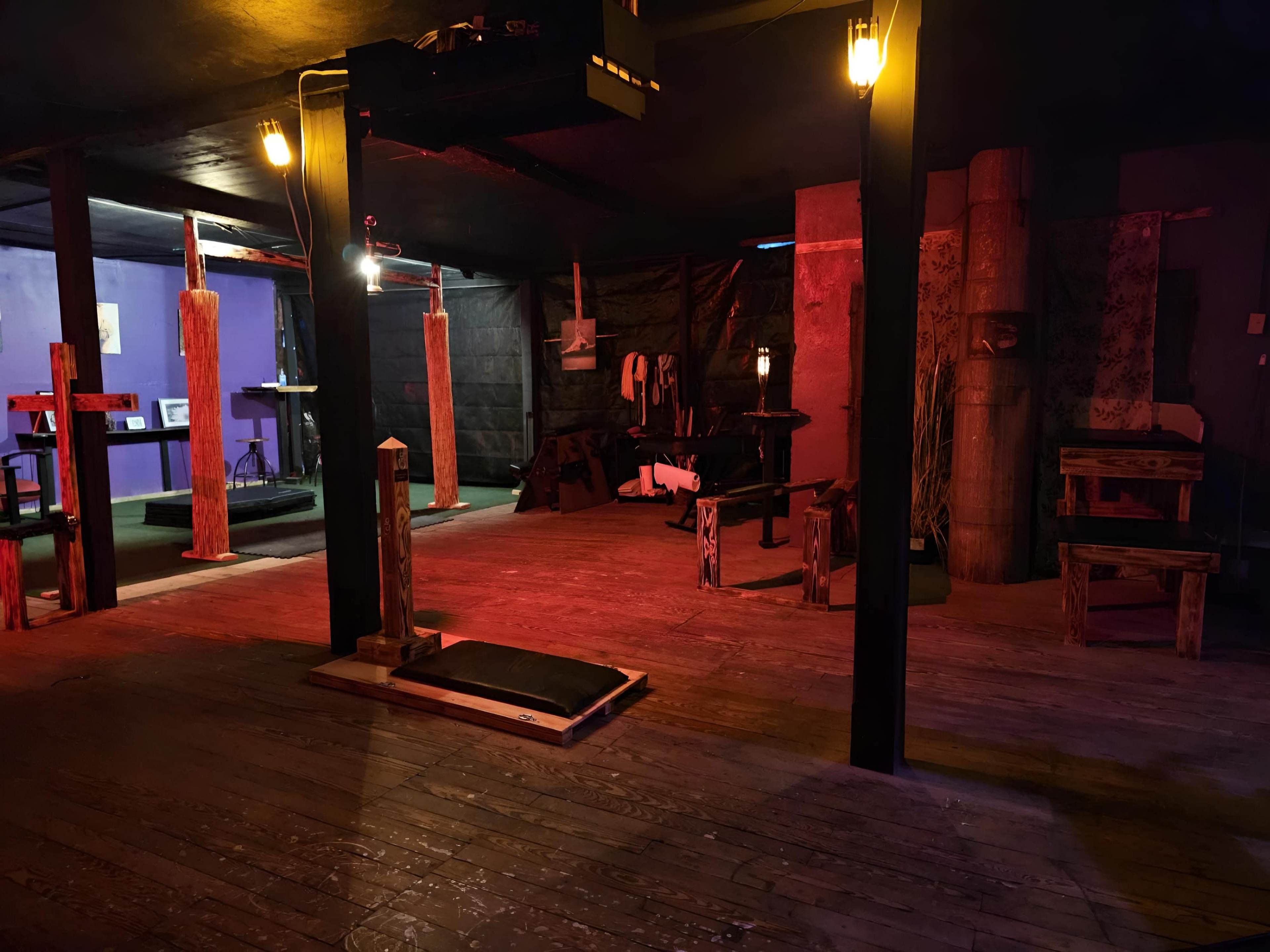 A dimly lit, rustic room with wooden structures and equipment arranged on the floor, illuminated by low red and orange lighting.