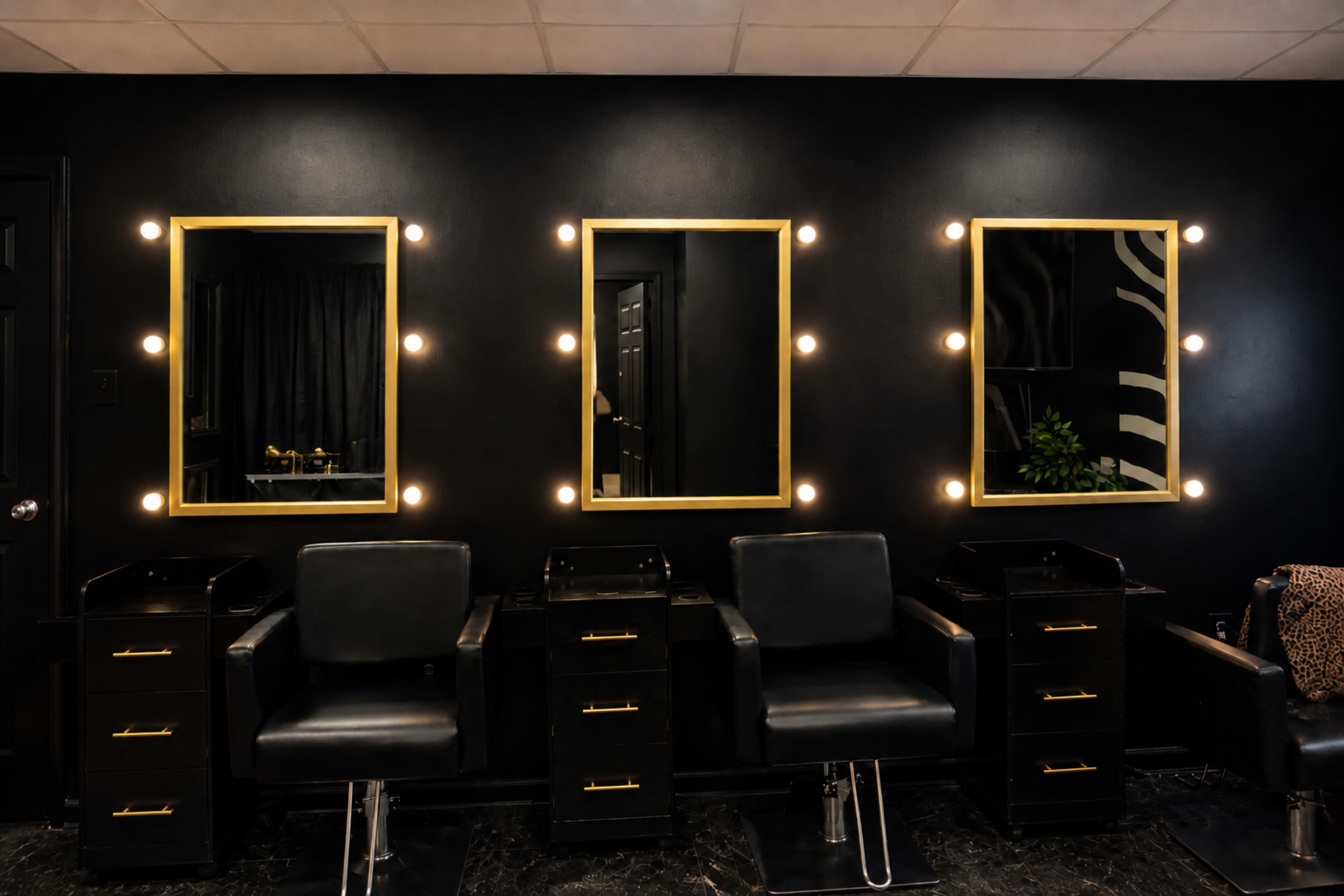 The image shows a modern hair salon interior with three mirrors framed in gold, bright light bulbs, and black styling chairs.