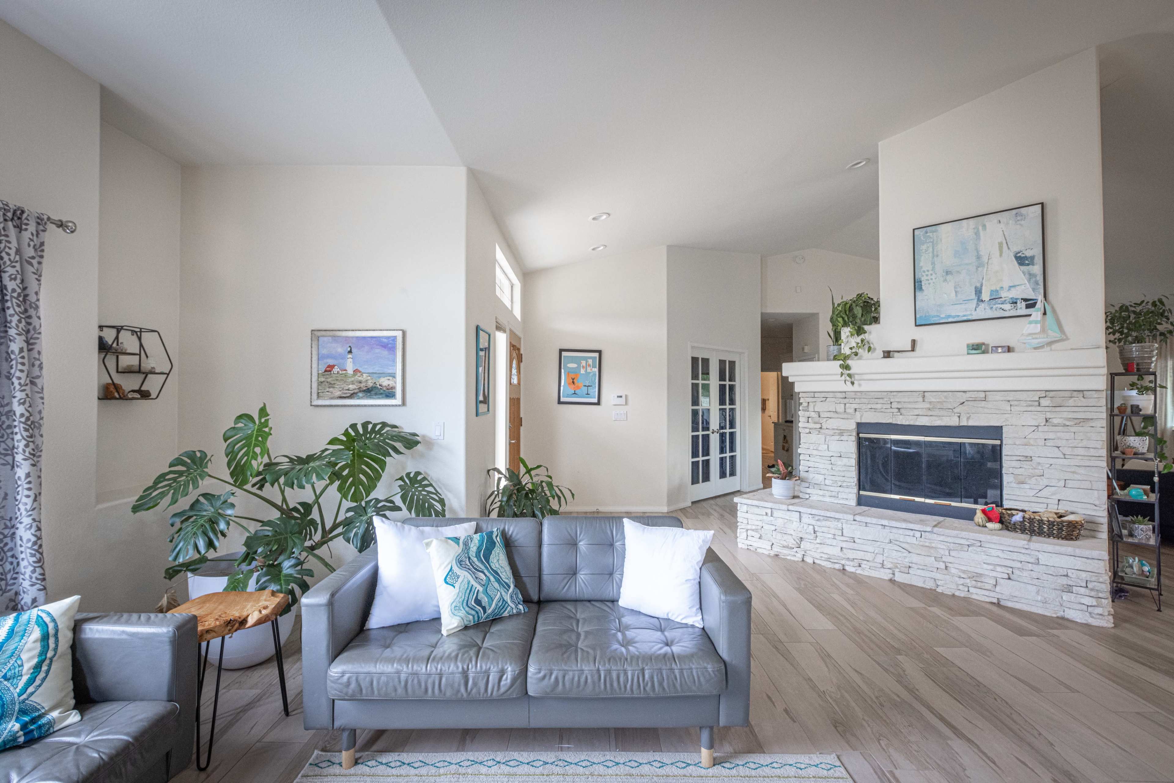 The image shows a modern living room with a gray leather sofa, a stone fireplace, and large windows allowing natural light.
