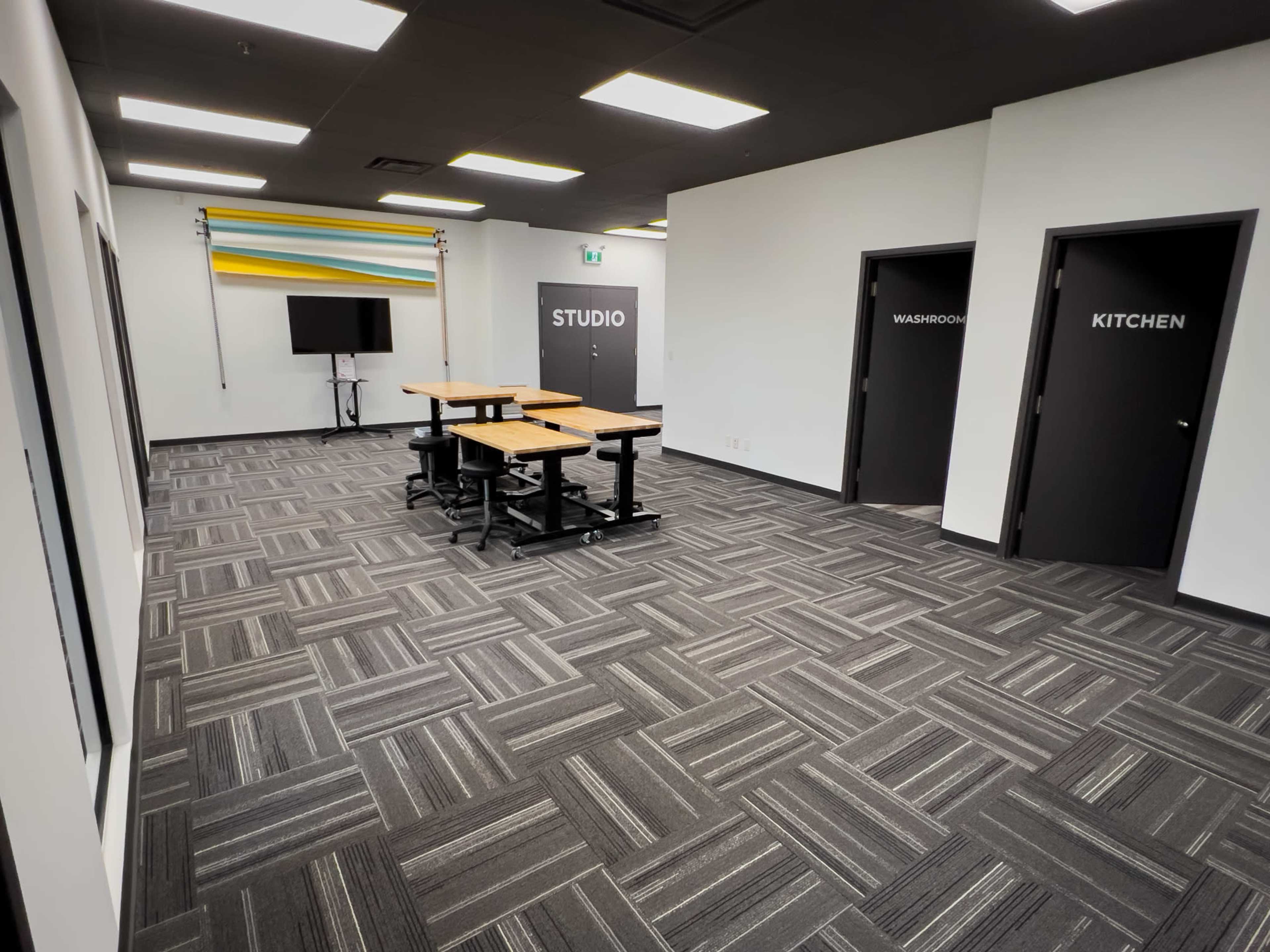 A modern workspace with two doors labeled "WASHROOM" and "KITCHEN," a table in the center, and a wall decorated with colorful stripes.