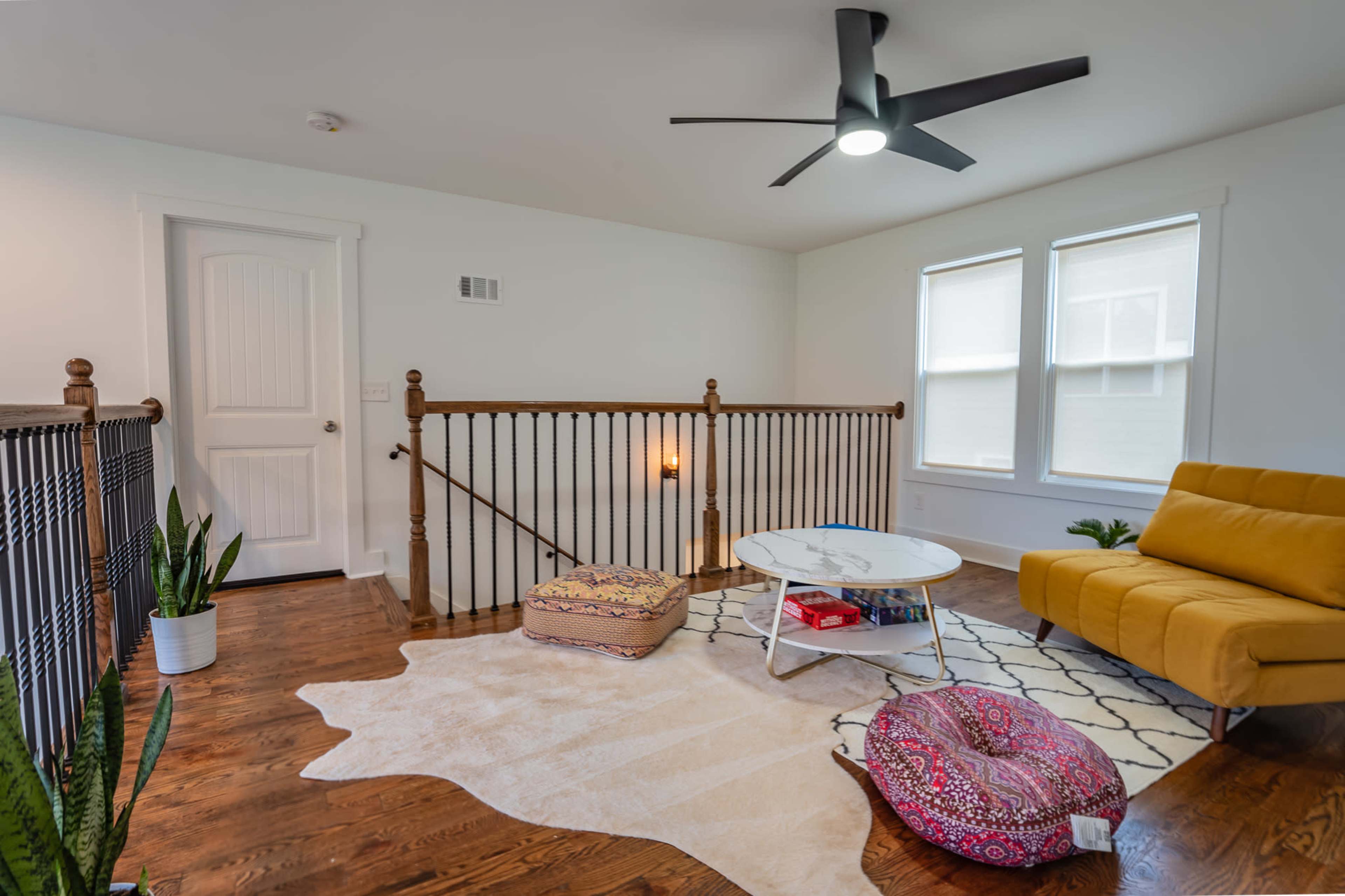A modern upstairs living area with a yellow couch, a round coffee table, and a patterned rug on wooden flooring.
