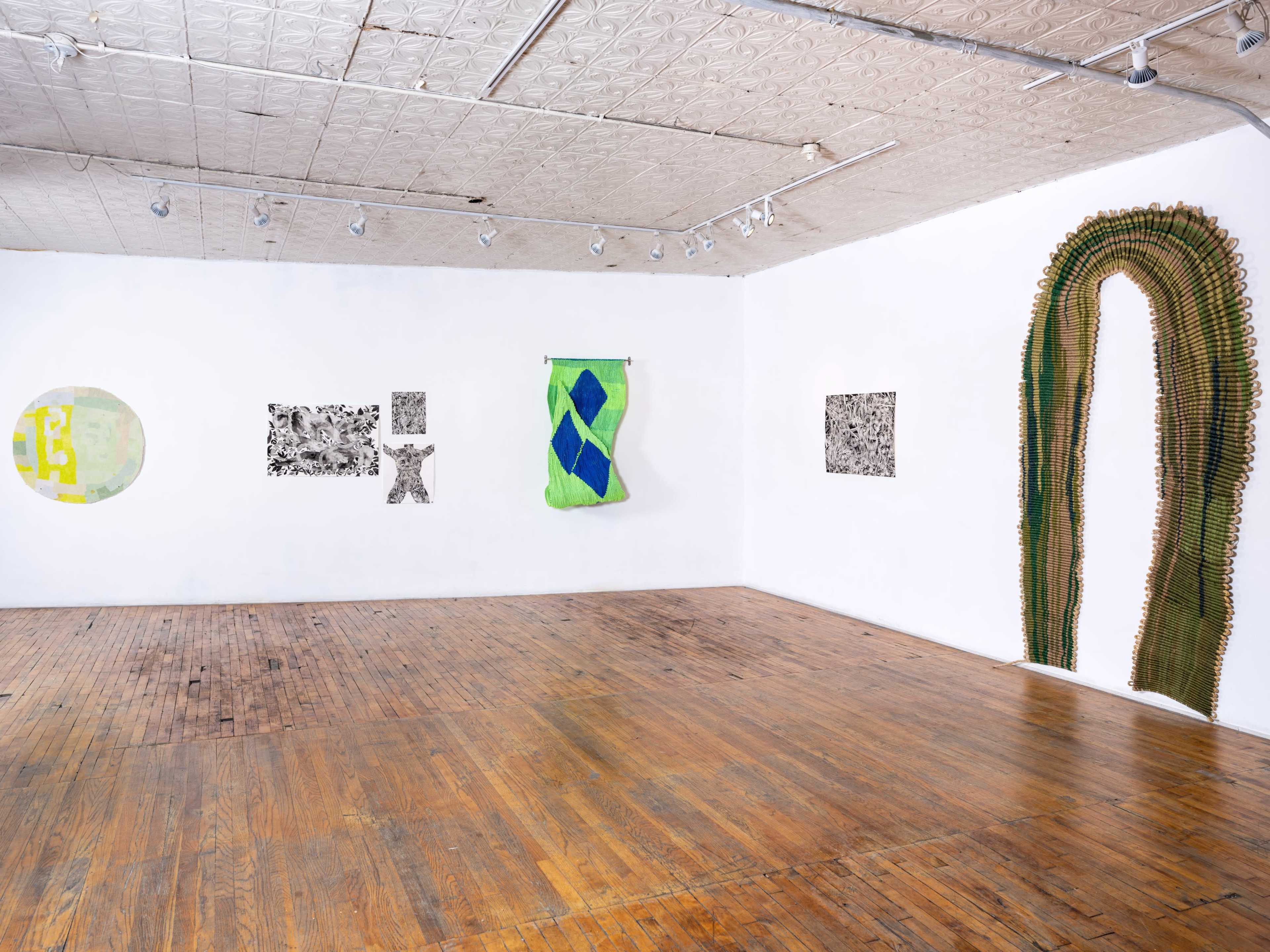 An art gallery features several abstract artworks displayed on white walls, with a wooden floor visible in the space.
