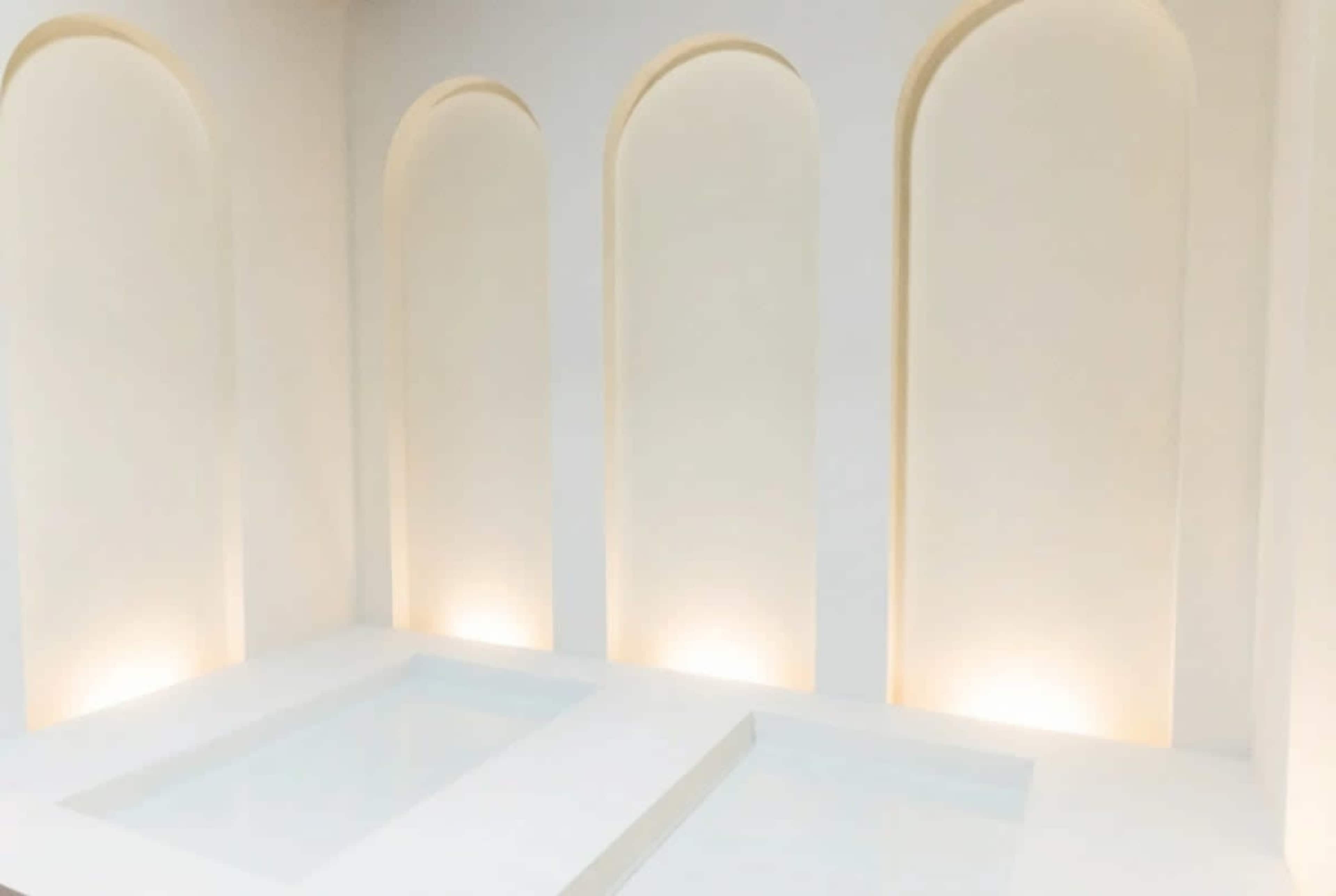 The image features a minimalist interior space with three arched niches and two shallow basins, all in light-colored tones.
