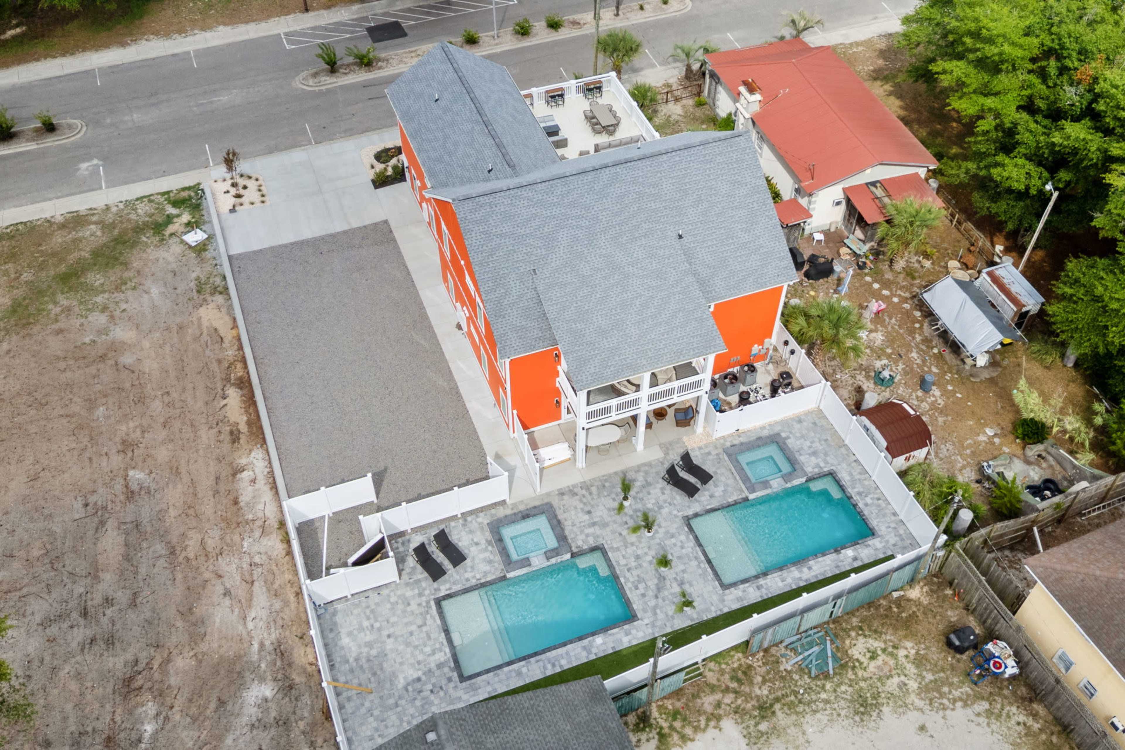 The image shows a two-story, brightly colored orange building with two swimming pools in a landscaped area, surrounded by a paved patio.