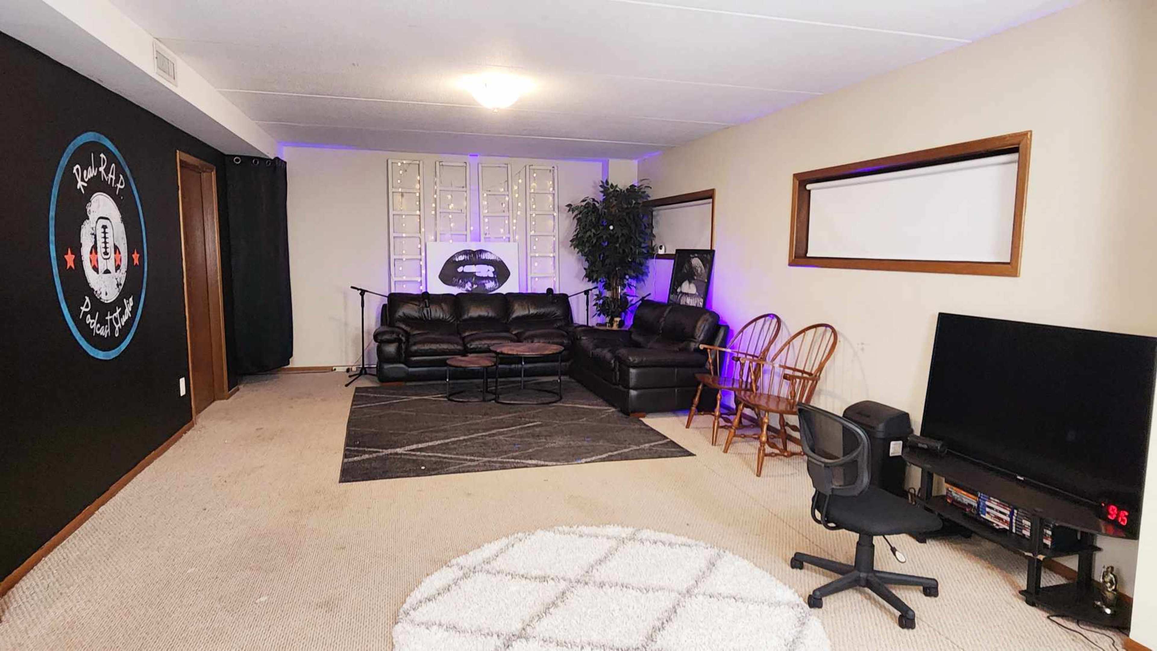 A spacious room with black and white walls, featuring a seating area with a black couch, a round coffee table, and a television in one corner.