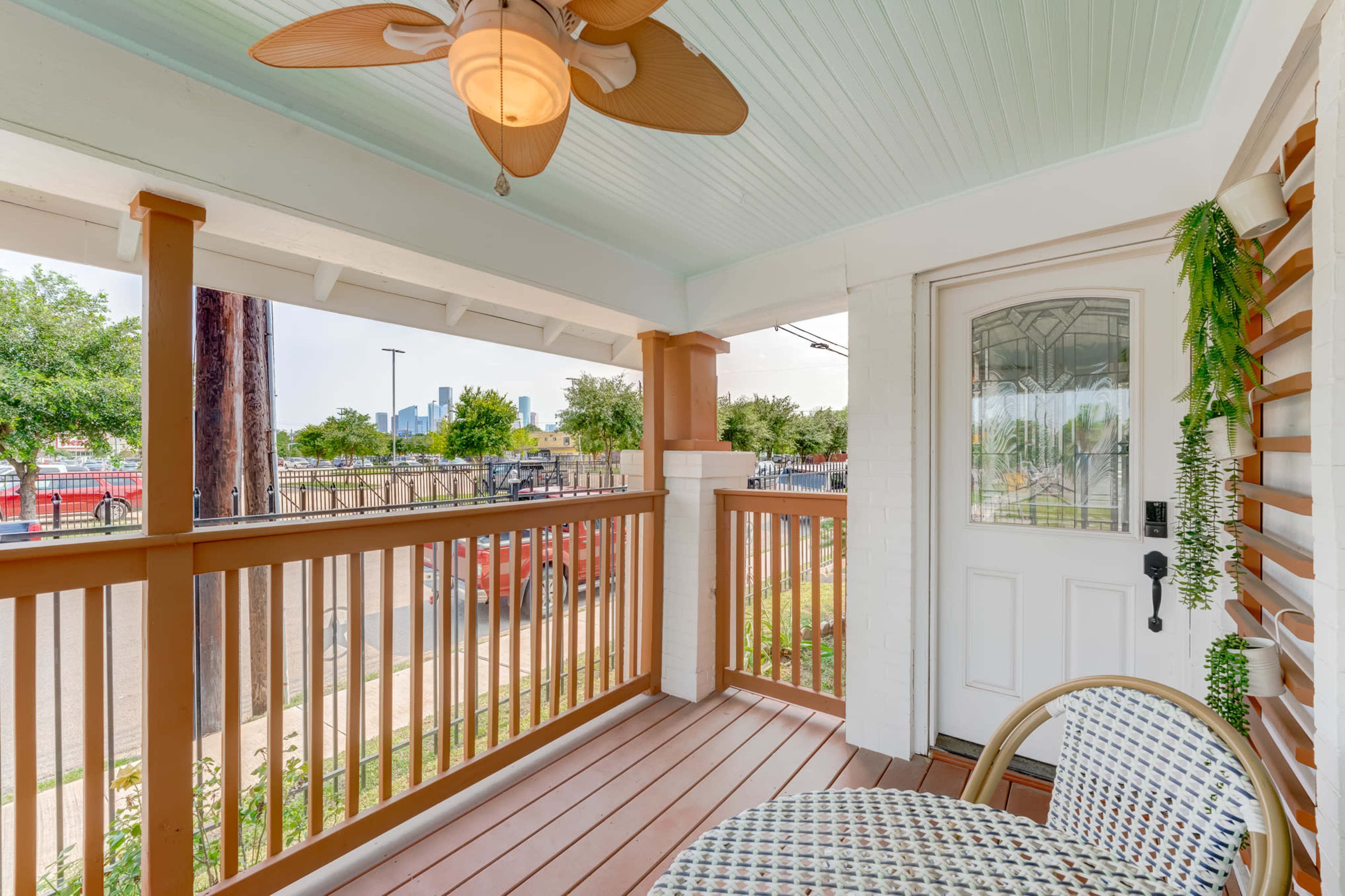 A covered porch features a ceiling fan, a small table with chairs, and a view of a city skyline in the distance.