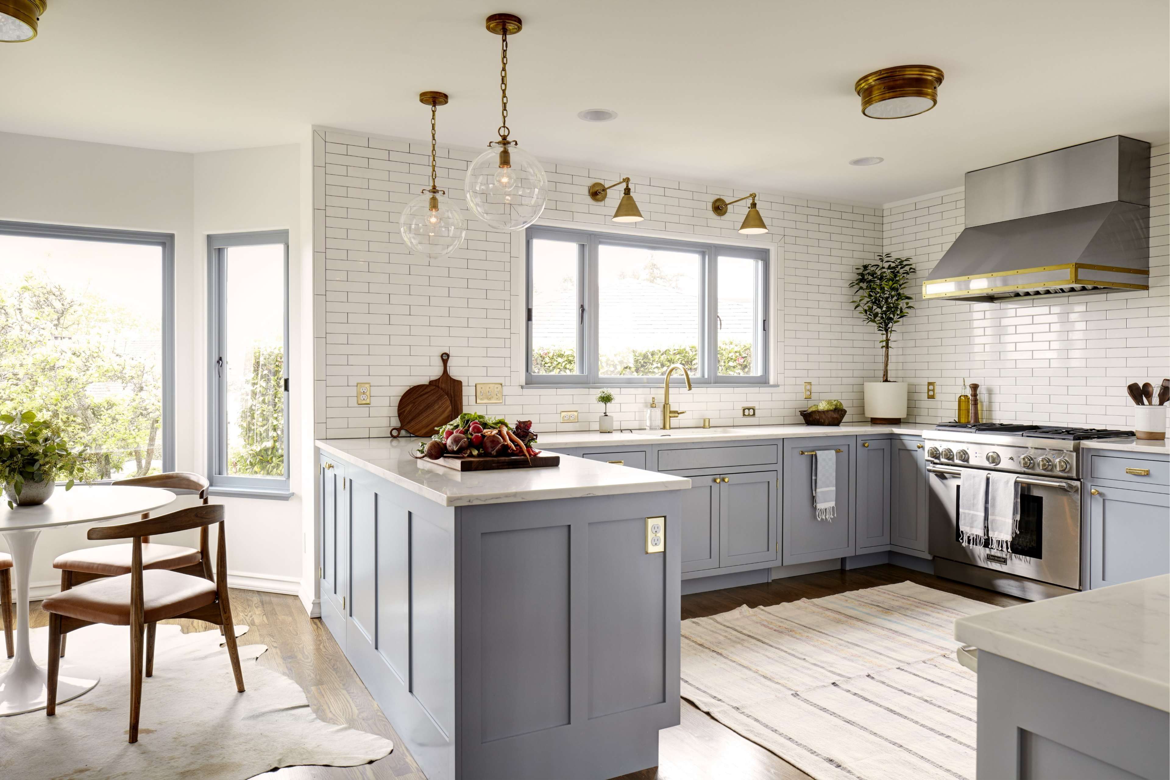A modern kitchen featuring light blue cabinets, a marble-topped island, stainless steel appliances, and large windows allowing natural light.
