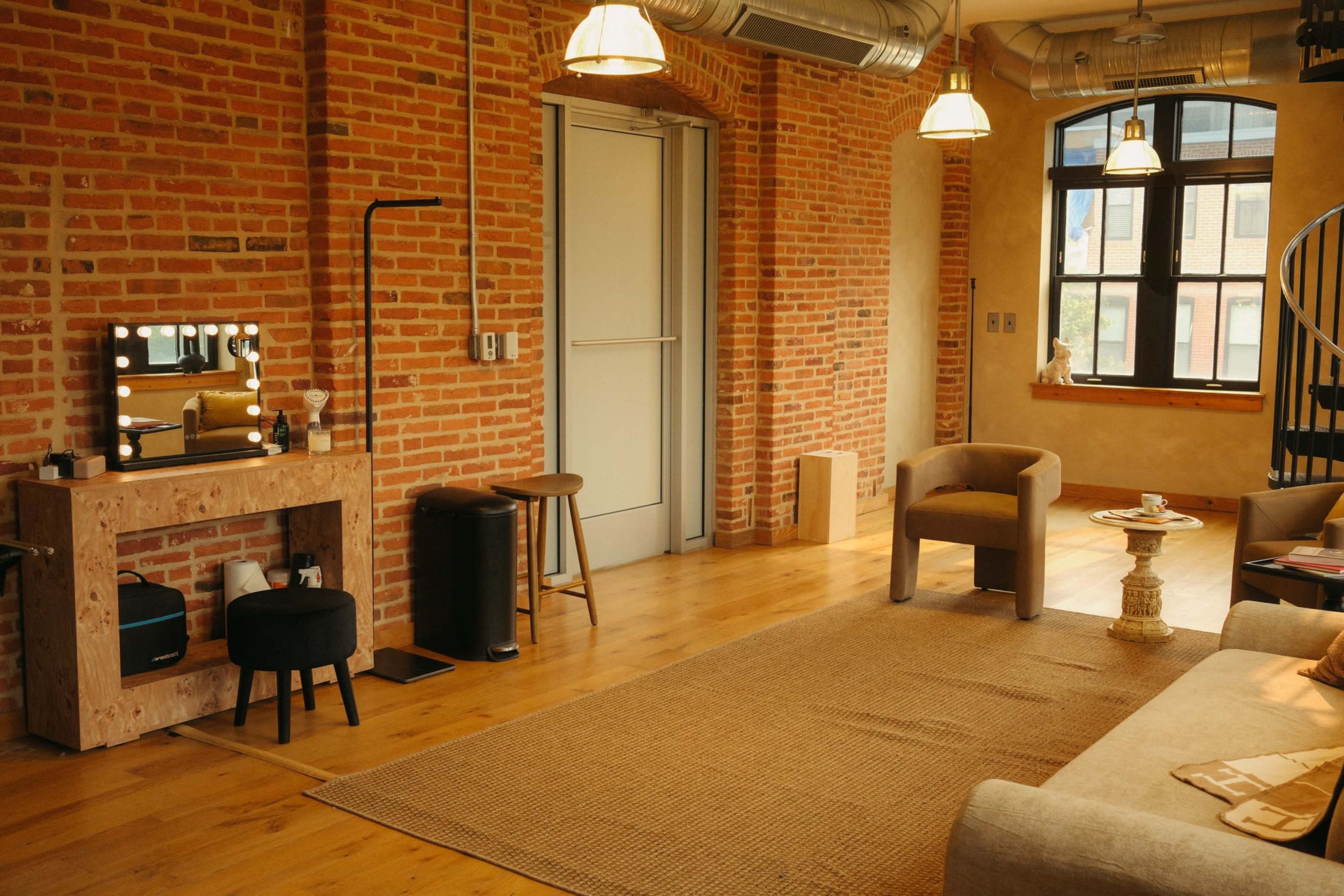 The image shows a spacious living room with exposed brick walls, wooden flooring, and a cozy seating area featuring a sofa and two armchairs.