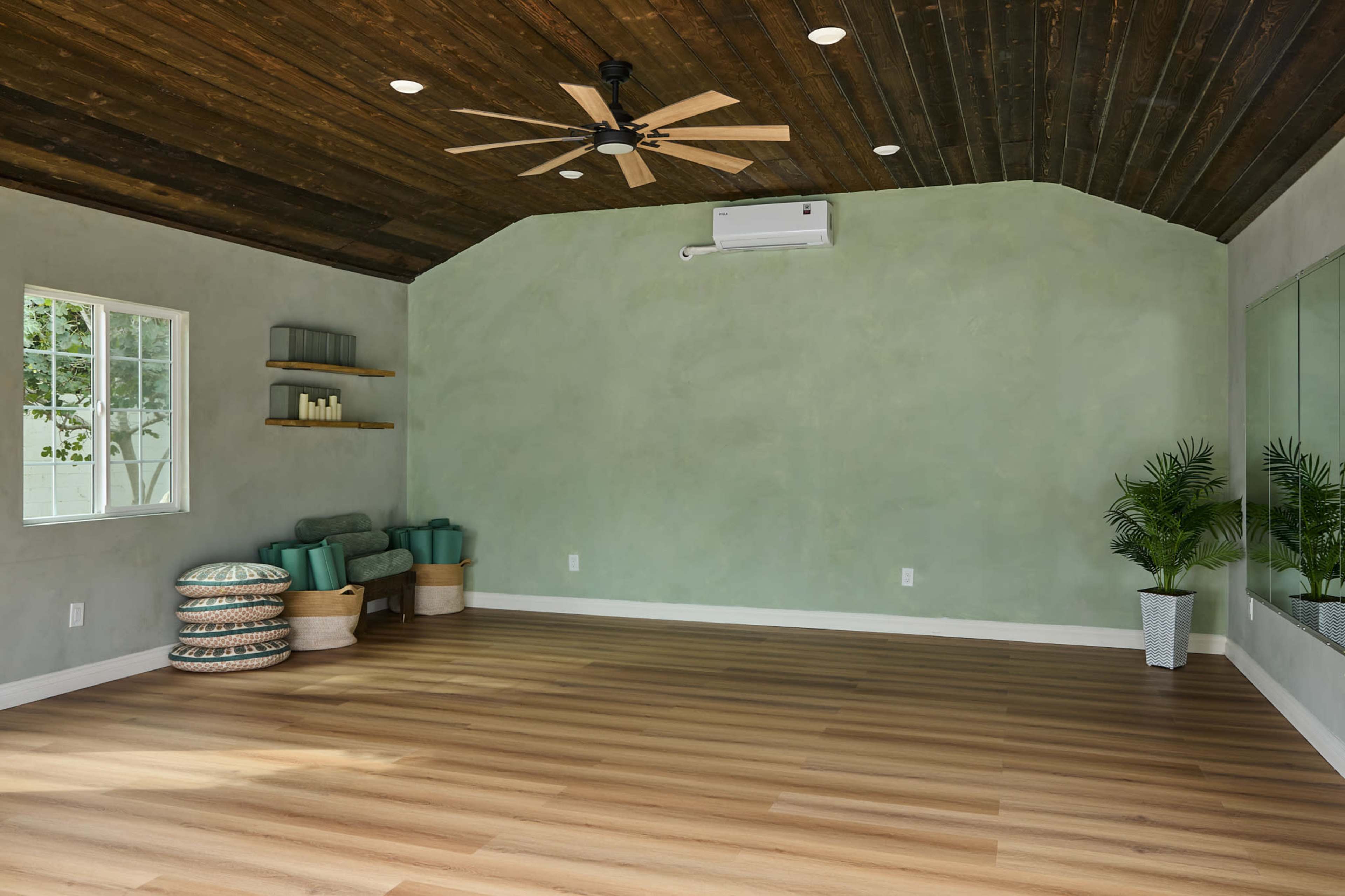 The room features a light green wall, wooden ceiling beams, a ceiling fan, wooden flooring, and minimal furnishings including a sofa and plants.