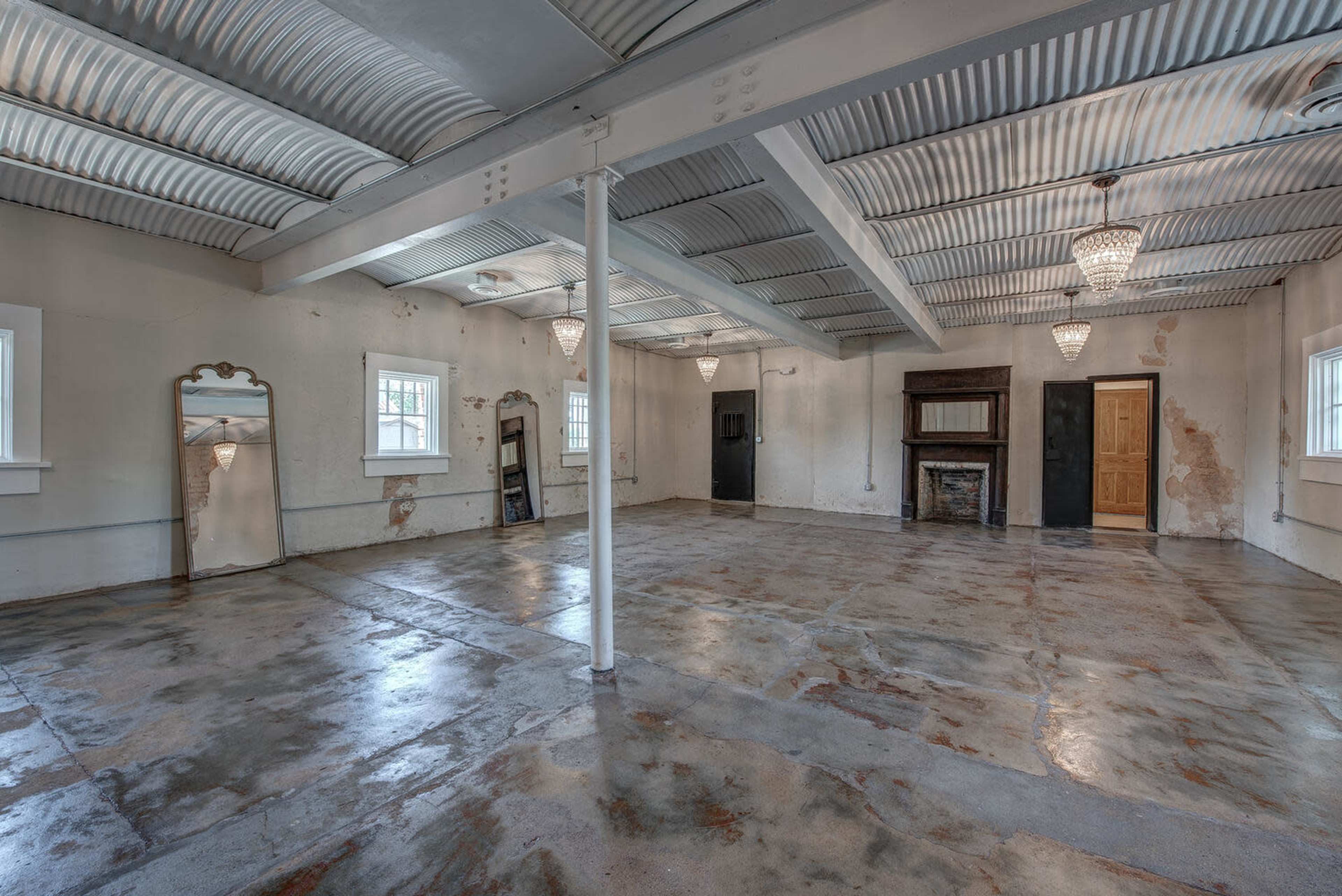 A spacious, unfinished room with concrete flooring, exposed beams, and several light fixtures.