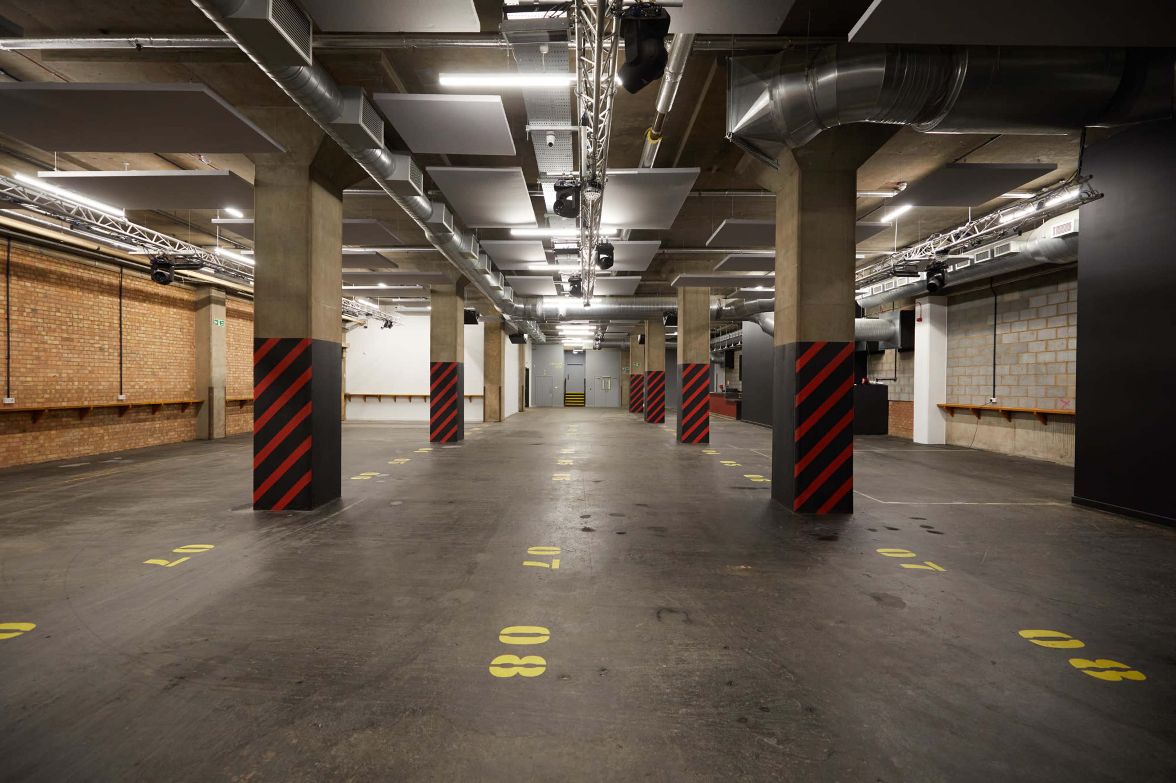 An empty underground parking garage with concrete pillars marked with black and red stripes and yellow floor markings.