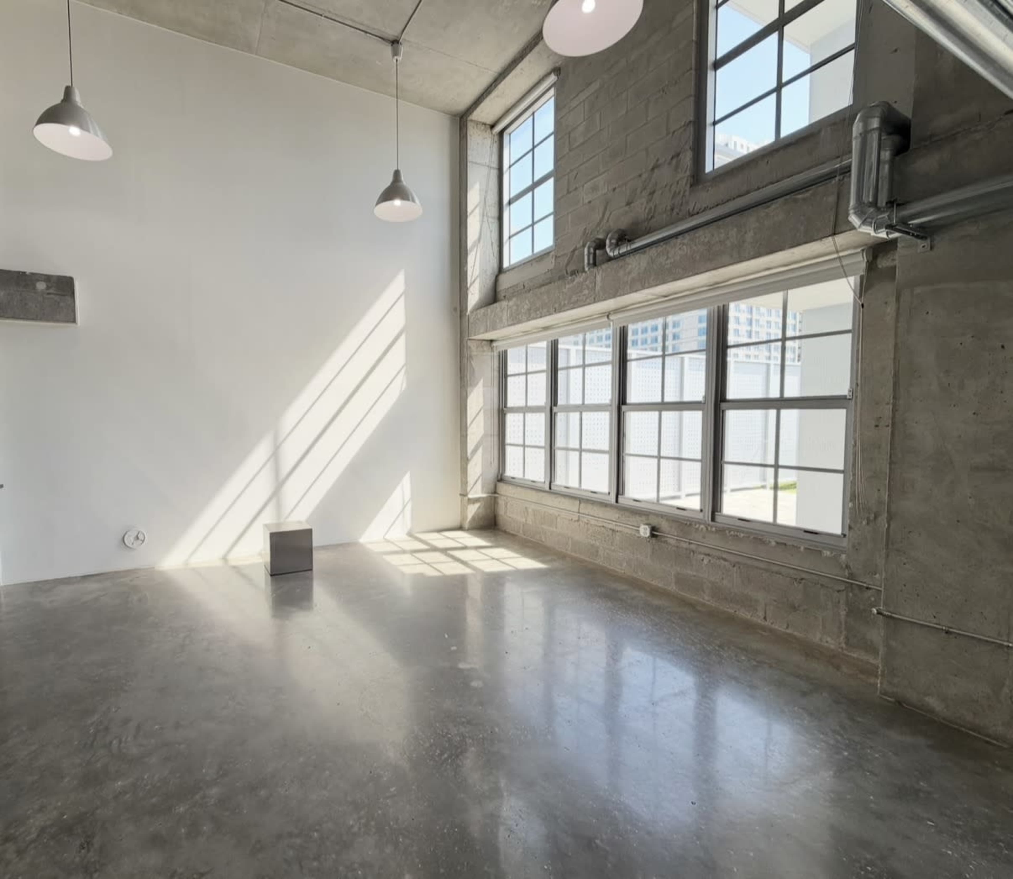 The image shows a spacious, well-lit interior with concrete walls, large windows, and polished floors.