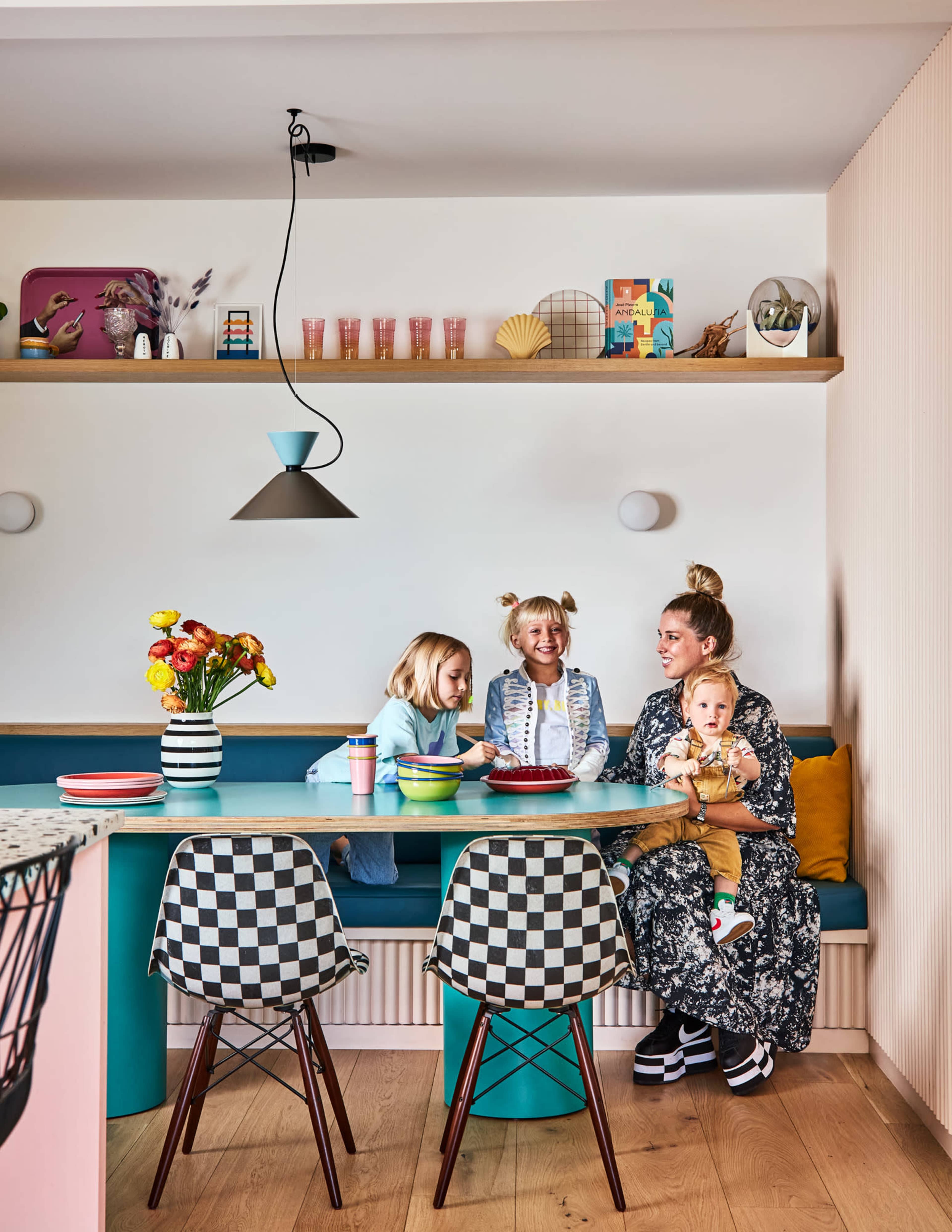 A family sits at a colorful dining table in a modern kitchen, with two adults and two children engaged in conversation and play.