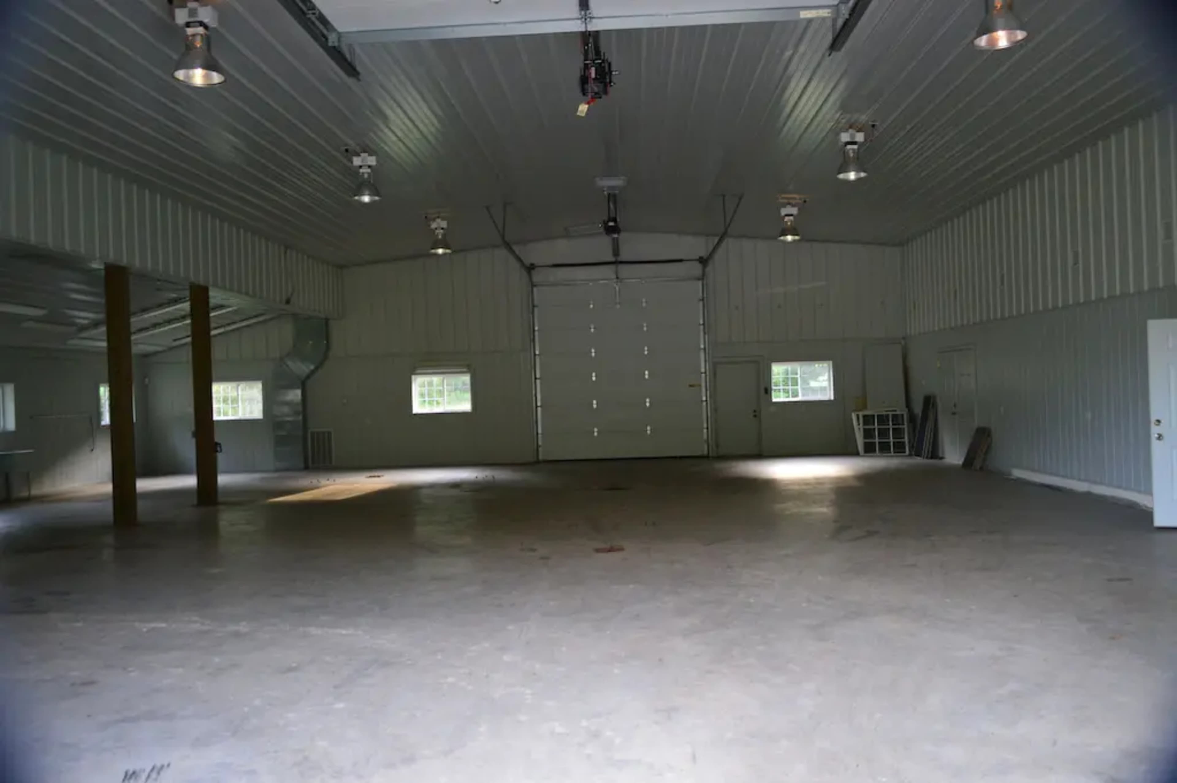 An empty metal-walled garage with a large overhead door and several lights illuminating the space.