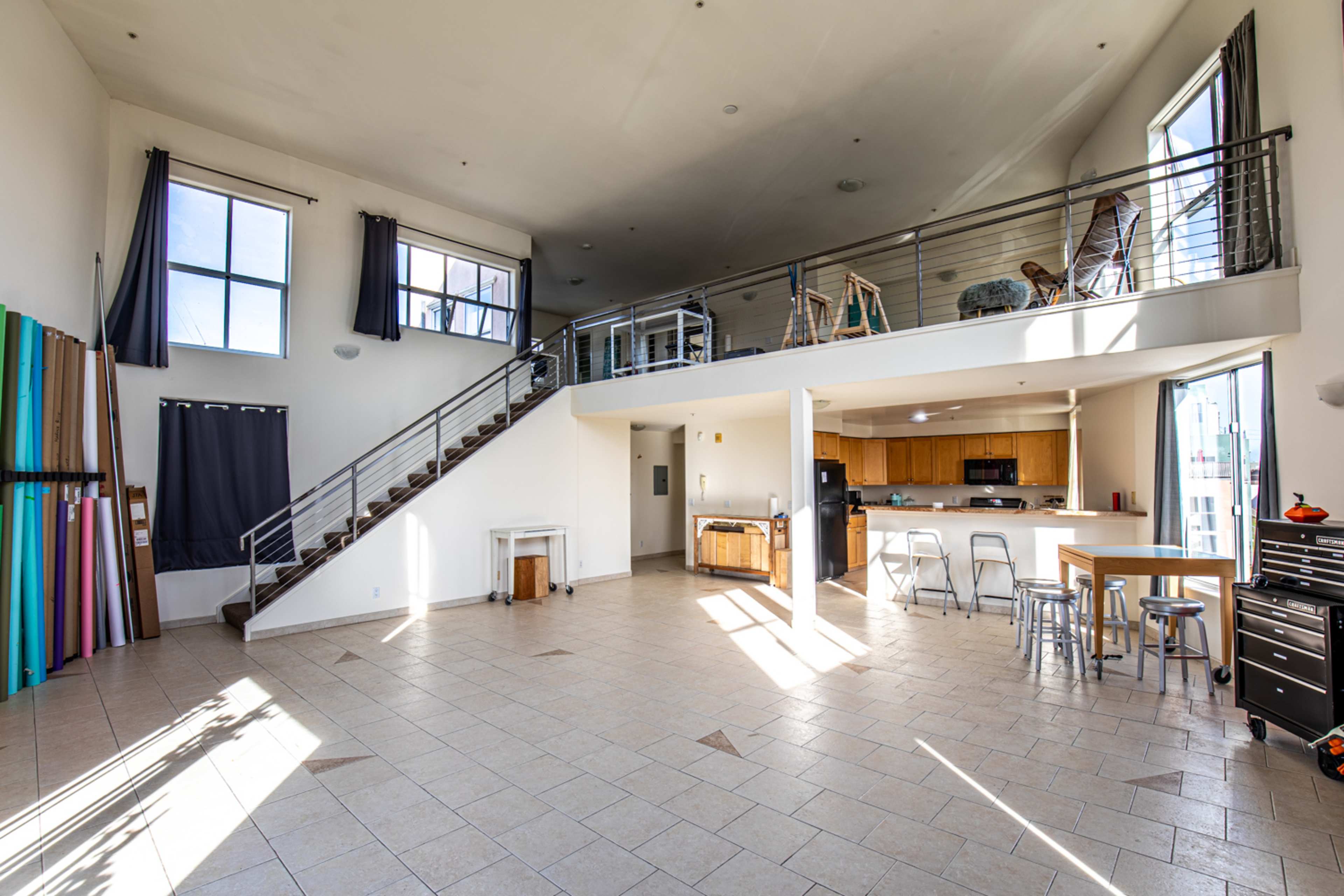 A spacious, modern interior with a staircase leading to a loft area, featuring large windows and a kitchen area with seating.