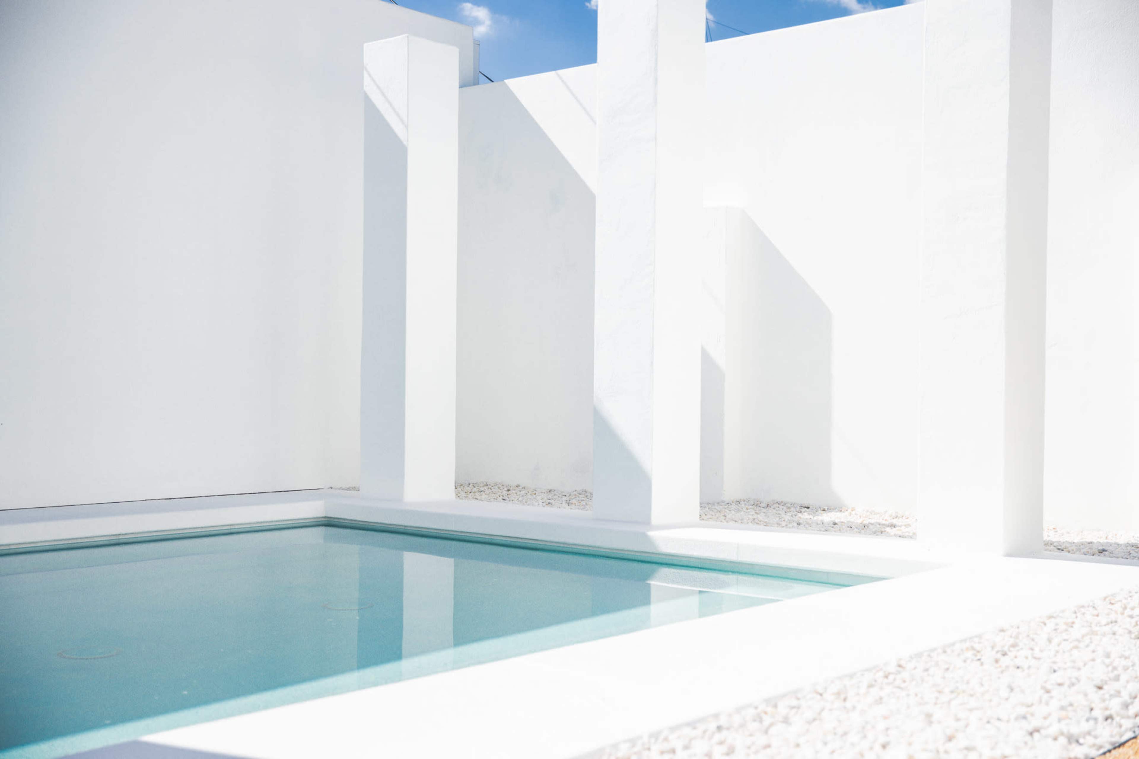 A minimalist courtyard with a clear pool surrounded by white walls and a gravel surface.
