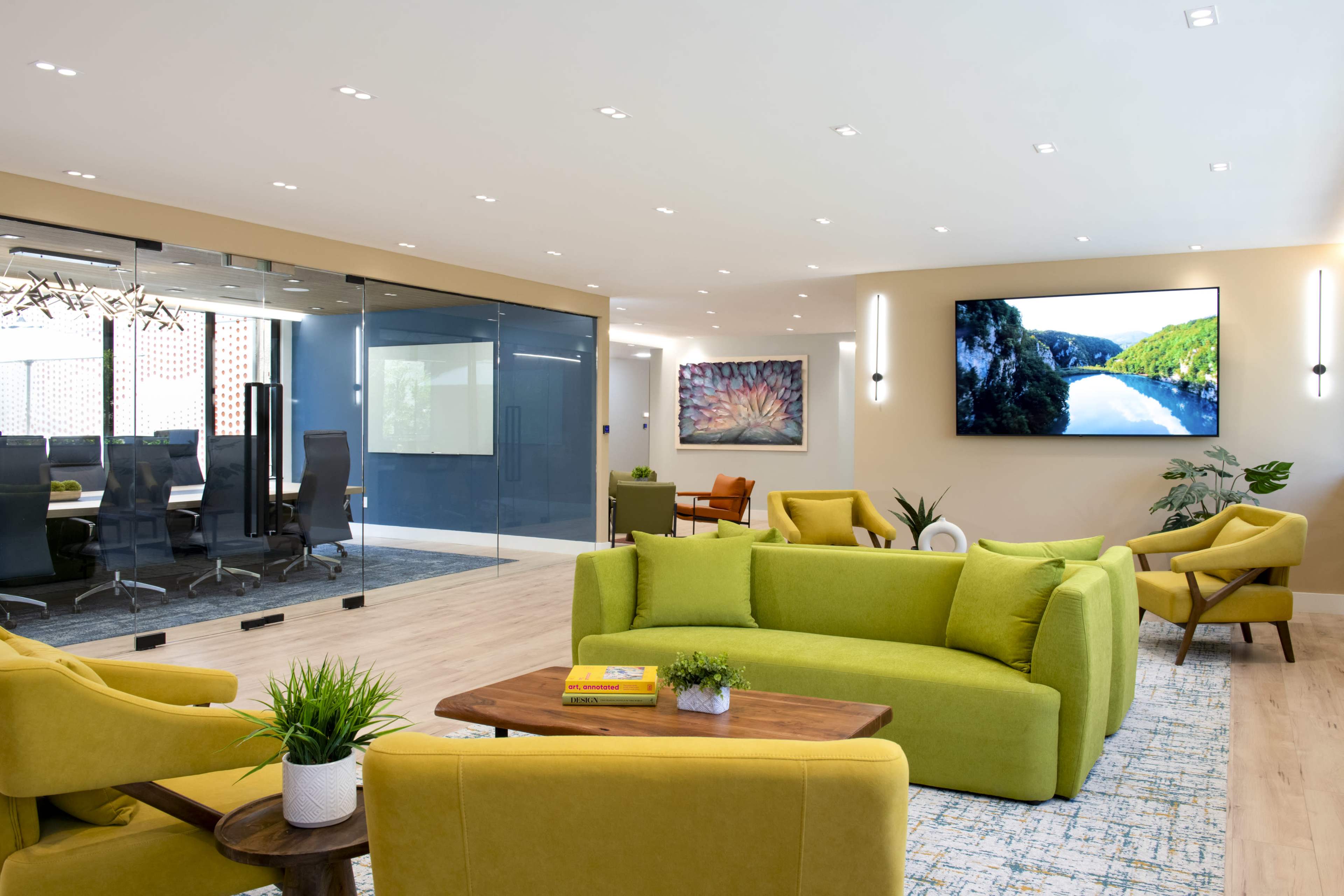 The scene features a modern office lounge area with bright green sofas, a wooden coffee table, and a large television displaying a scenic landscape.