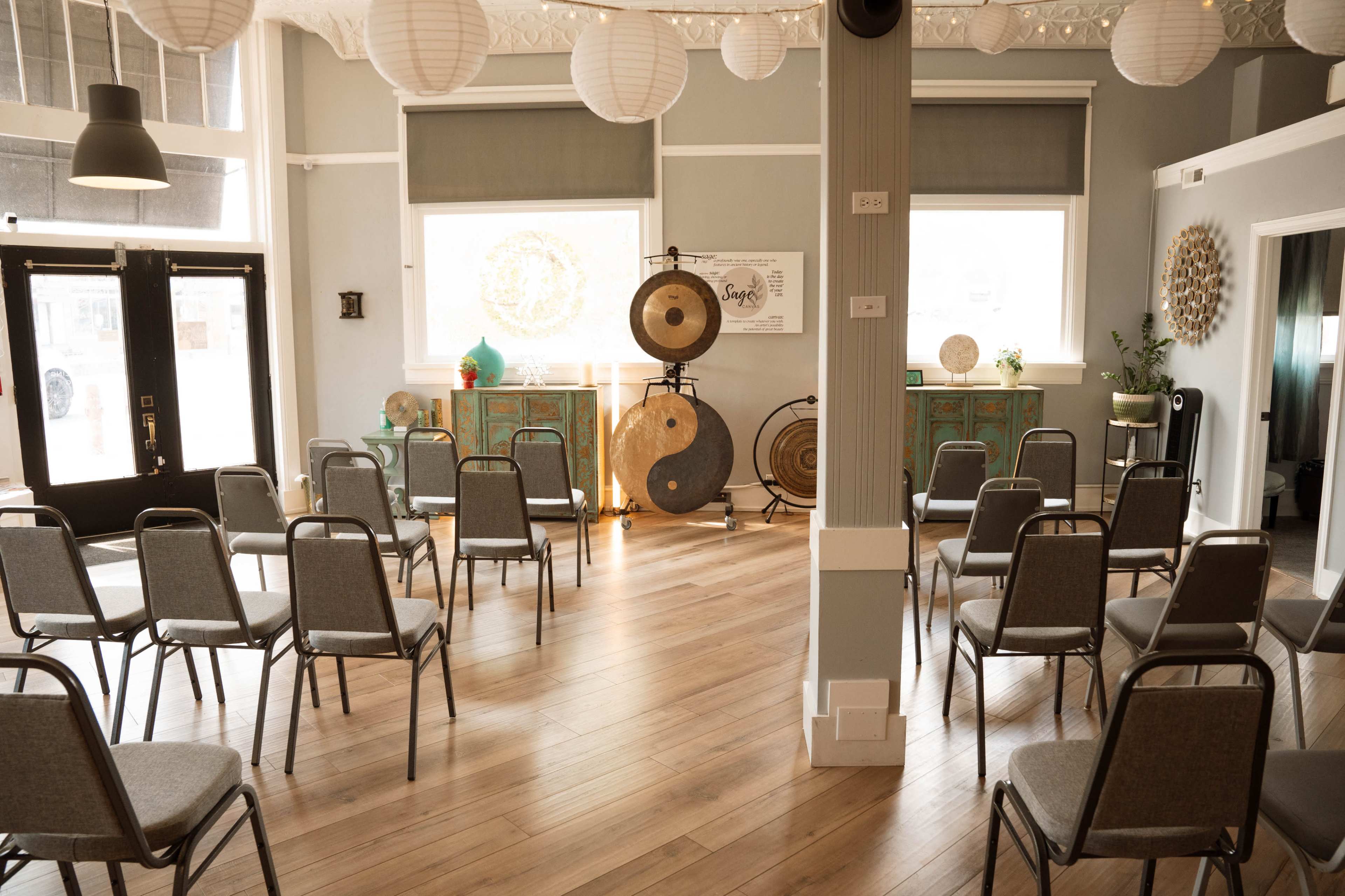 The image shows a spacious room arranged with gray chairs facing a decorative area featuring gongs and green furnishings.